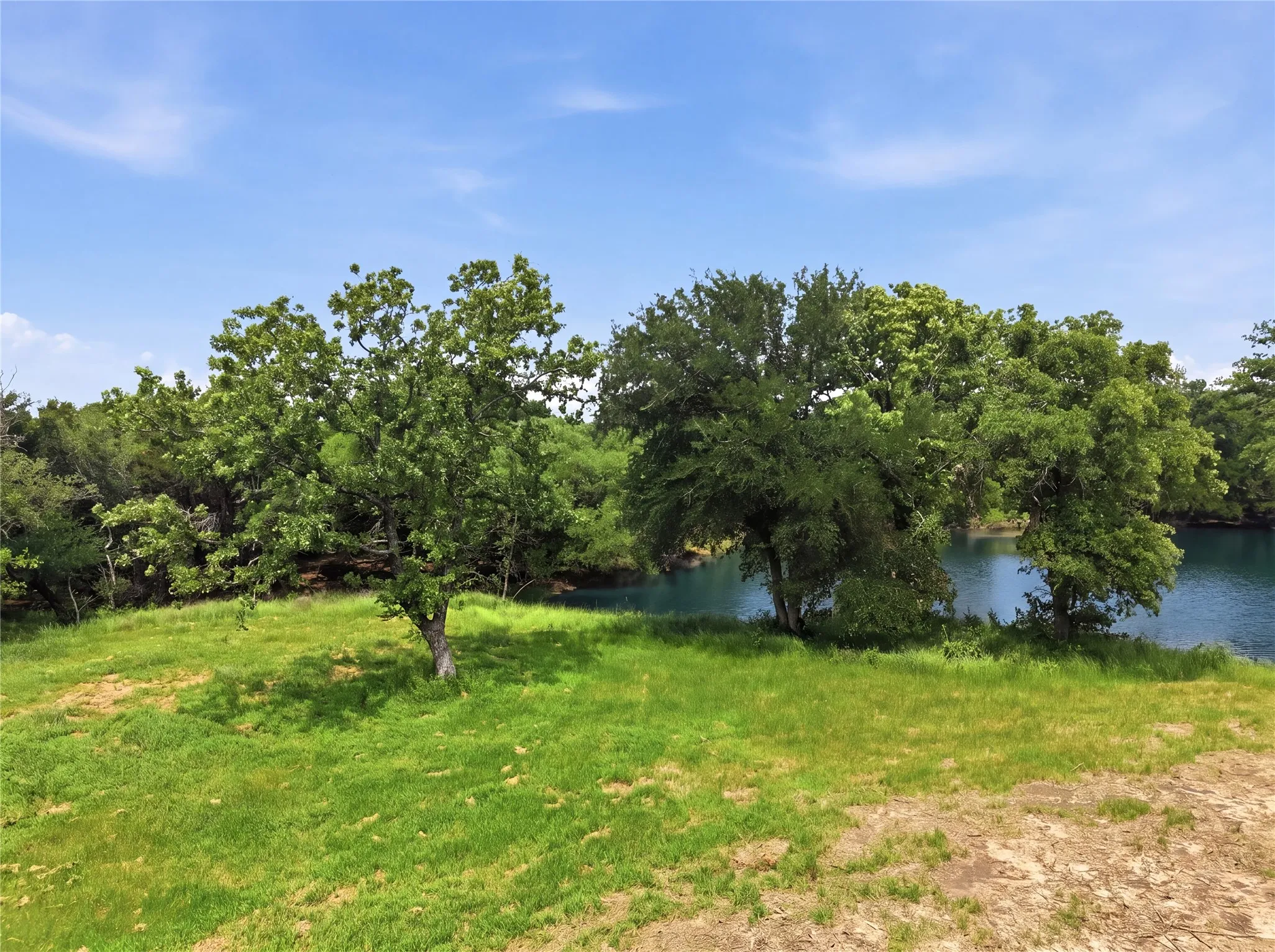 Expansive grassy area featuring mature trees and a tranquil body of water