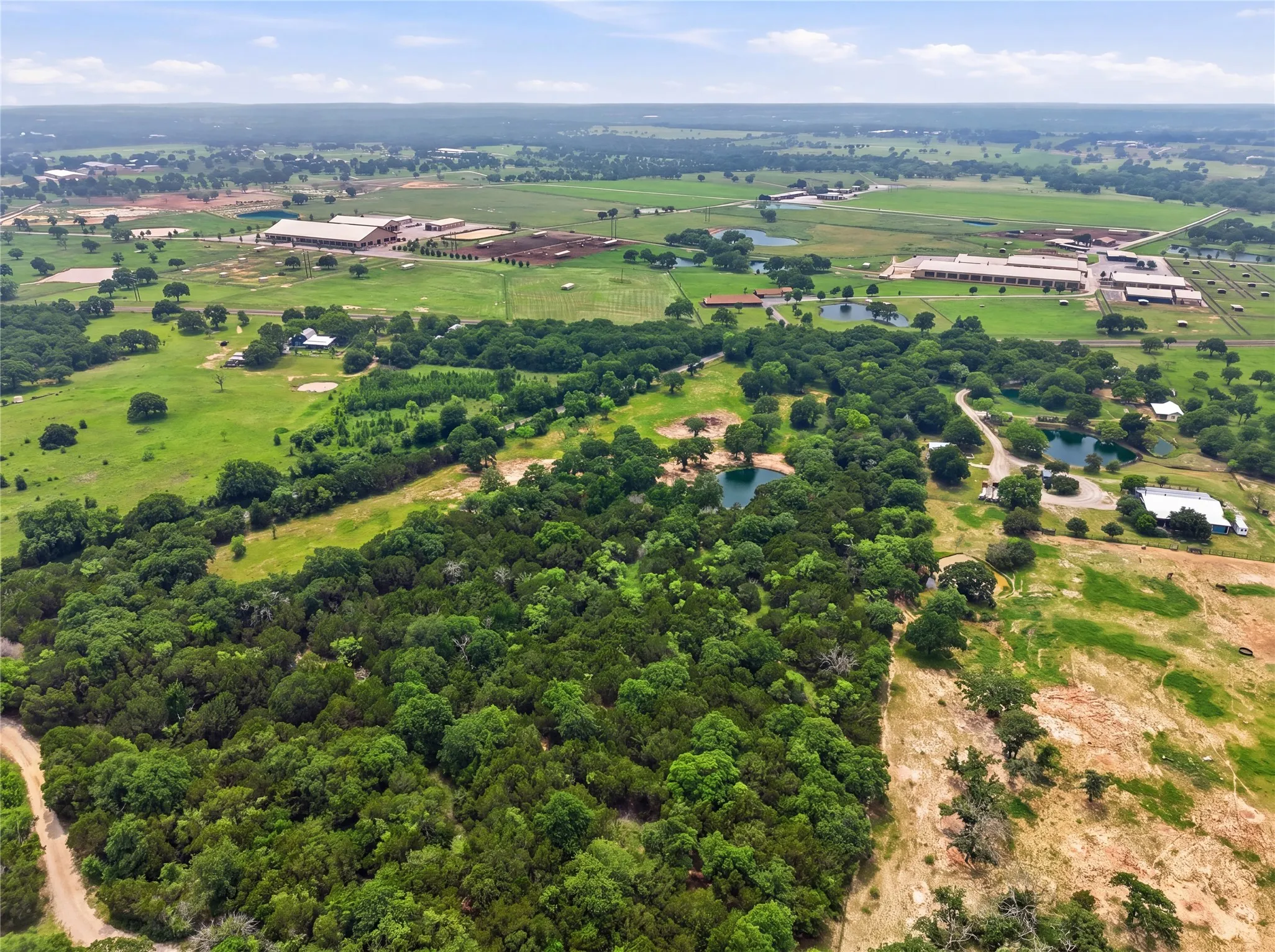 Expansive acreage featuring dense woodlands, open pastures, multiple ponds, and distant agricultural structures