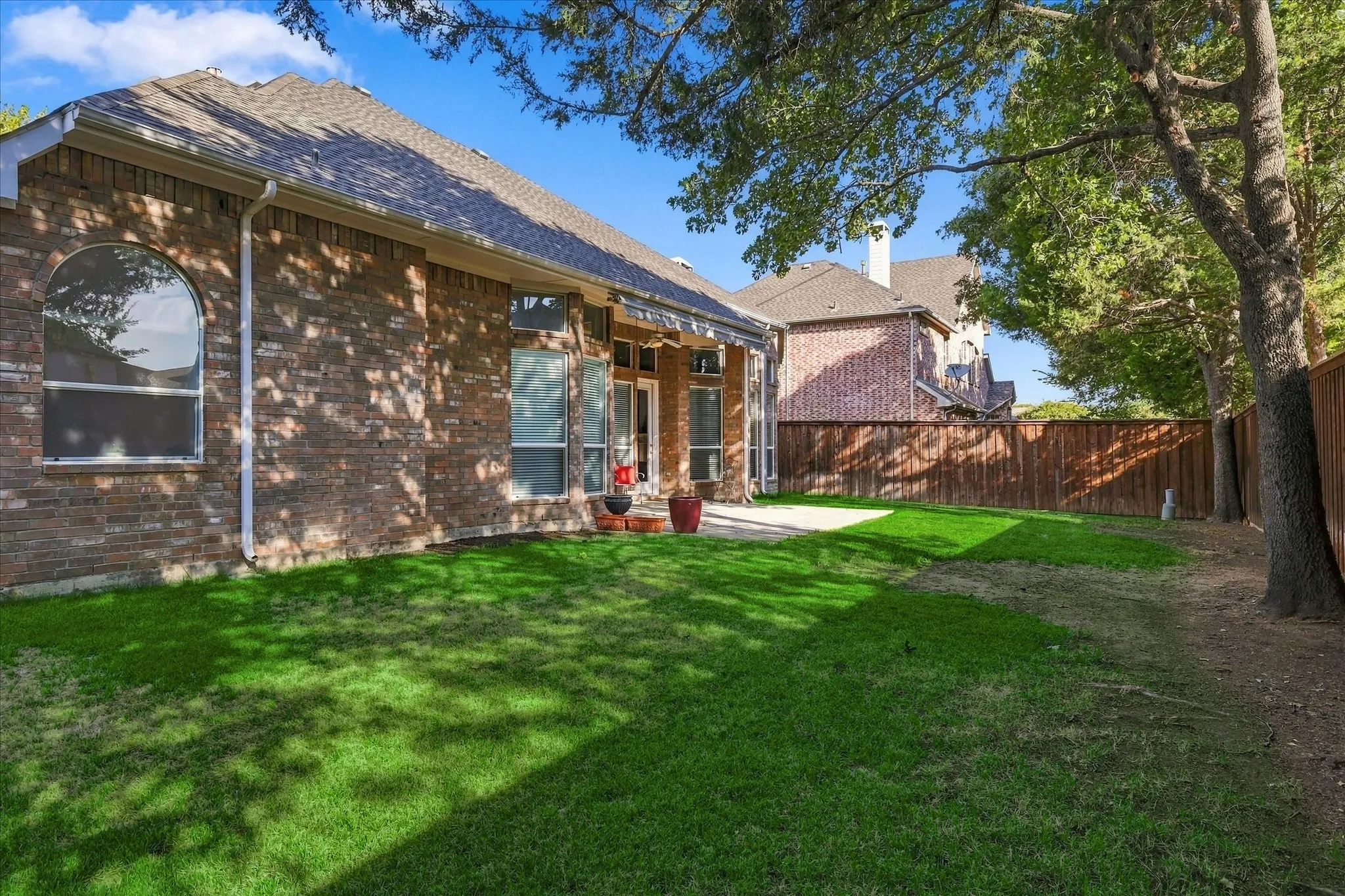 Expansive backyard with a manicured lawn, full brick exterior, arched window, and a wood privacy fence