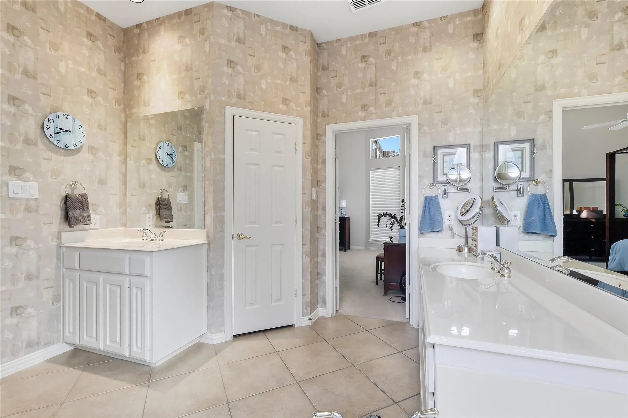 White dual vanity with integrated sinks, an arched window, a built-in soaking tub, tile flooring, and wall-mounted lighting