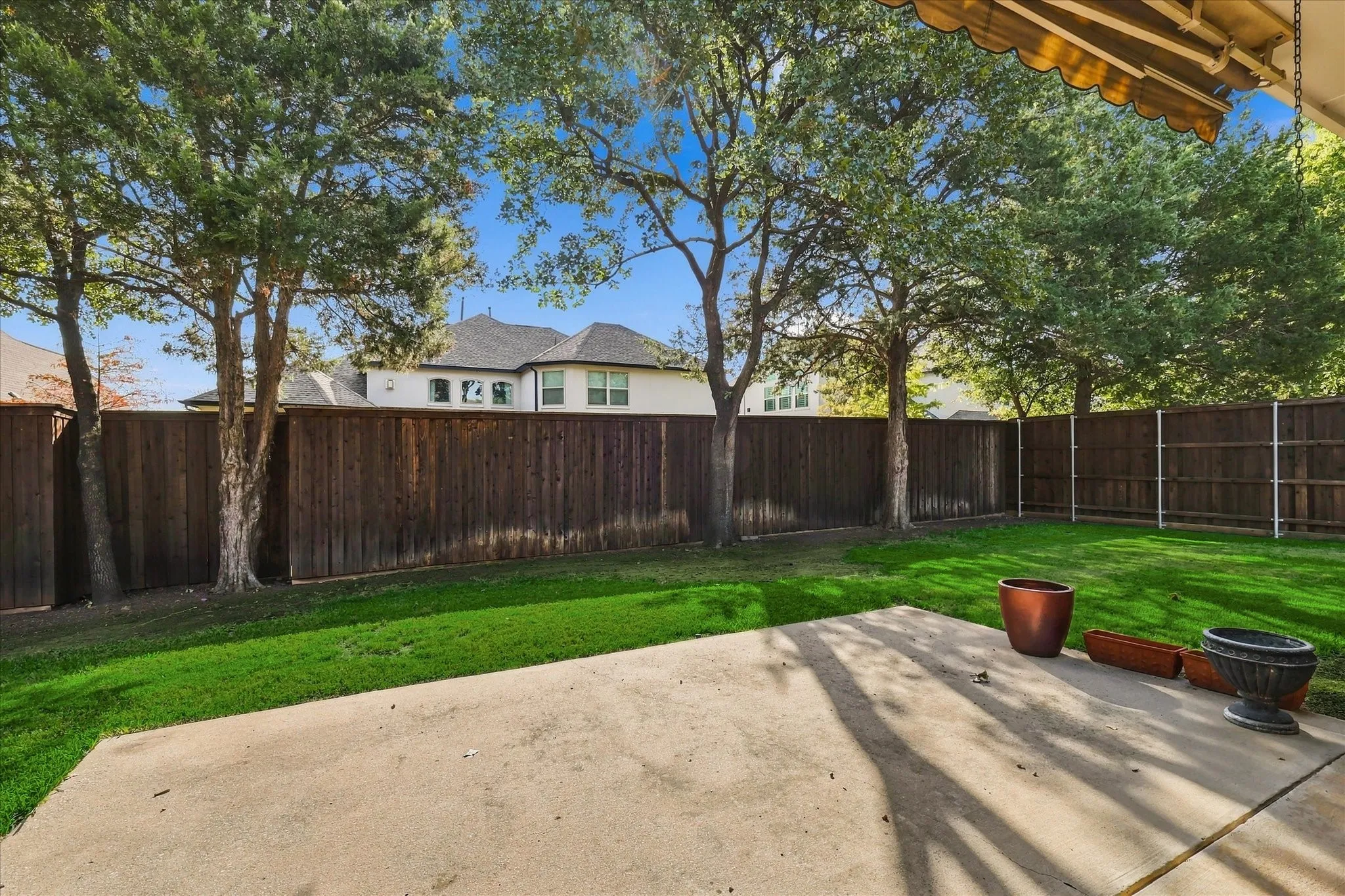Expansive backyard featuring a concrete patio, a manicured lawn, a privacy fence, and mature trees