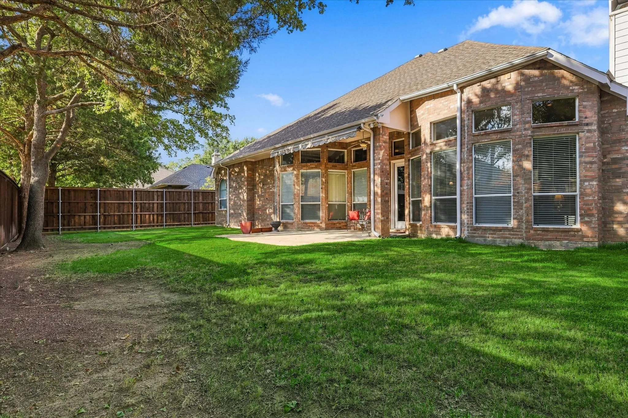 Brick exterior with multiple large windows, a private fenced yard, and a concrete patio