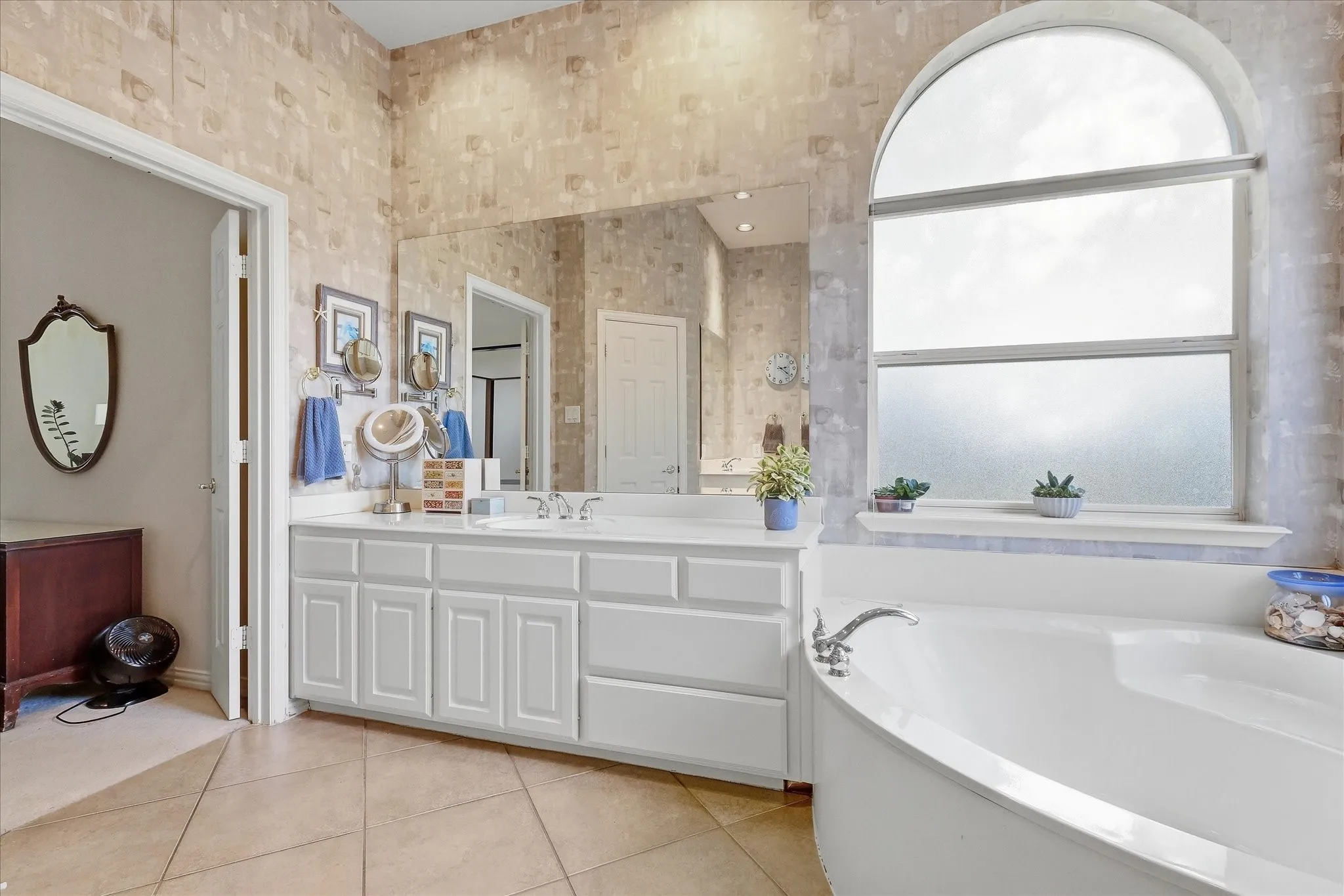 Arched window with frosted glass, built-in soaking tub, glass-enclosed shower with gold-tone frame, and tiled flooring