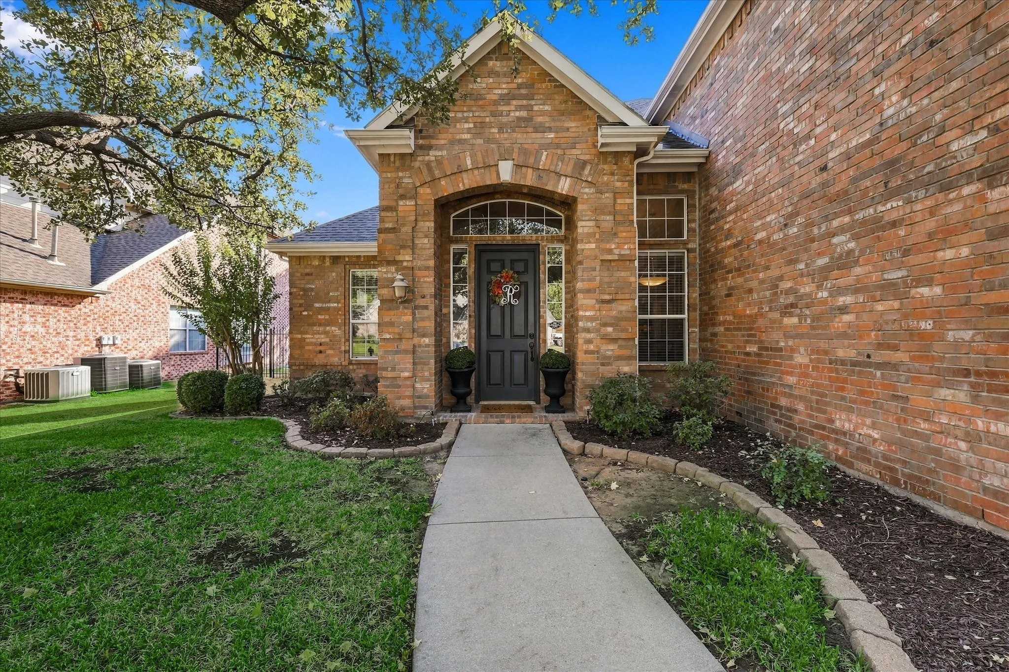 Welcoming brick exterior with arched entryway and sidelights, complemented by manicured landscaping and mature shade trees
