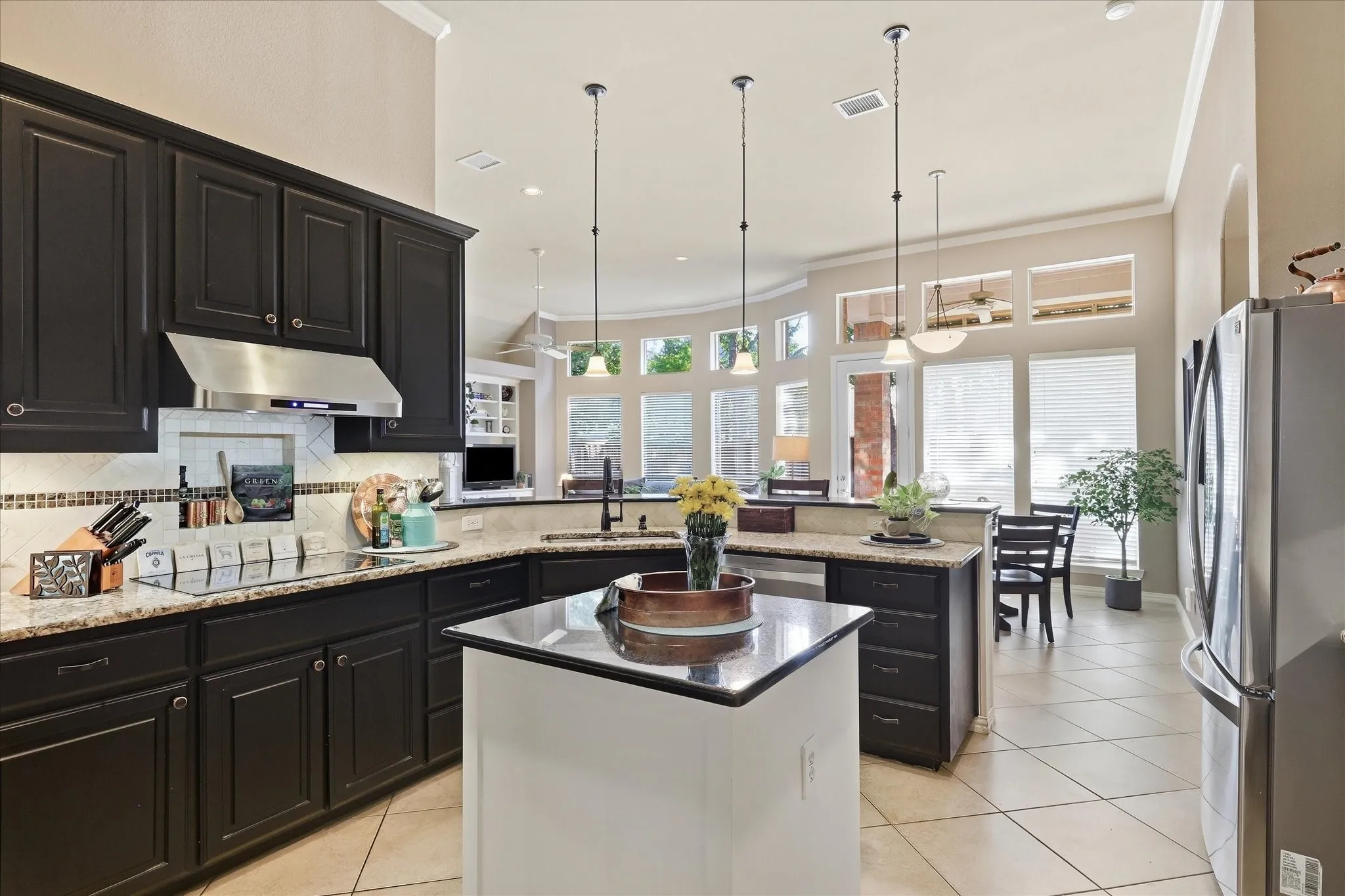 Kitchen featuring dark cabinetry, stainless steel appliances, a center island with pendant lighting, stone countertops, and tile flooring