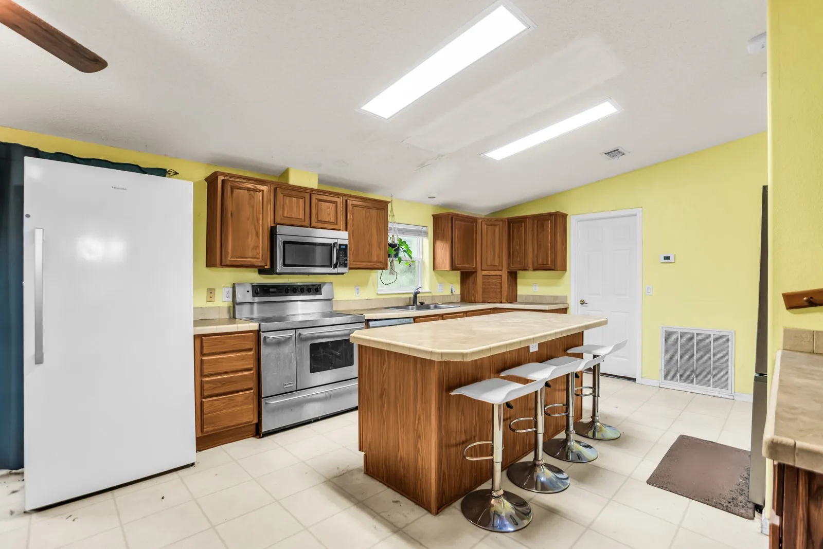 Kitchen featuring wood cabinetry, stainless steel appliances, a center island with seating, and tile flooring