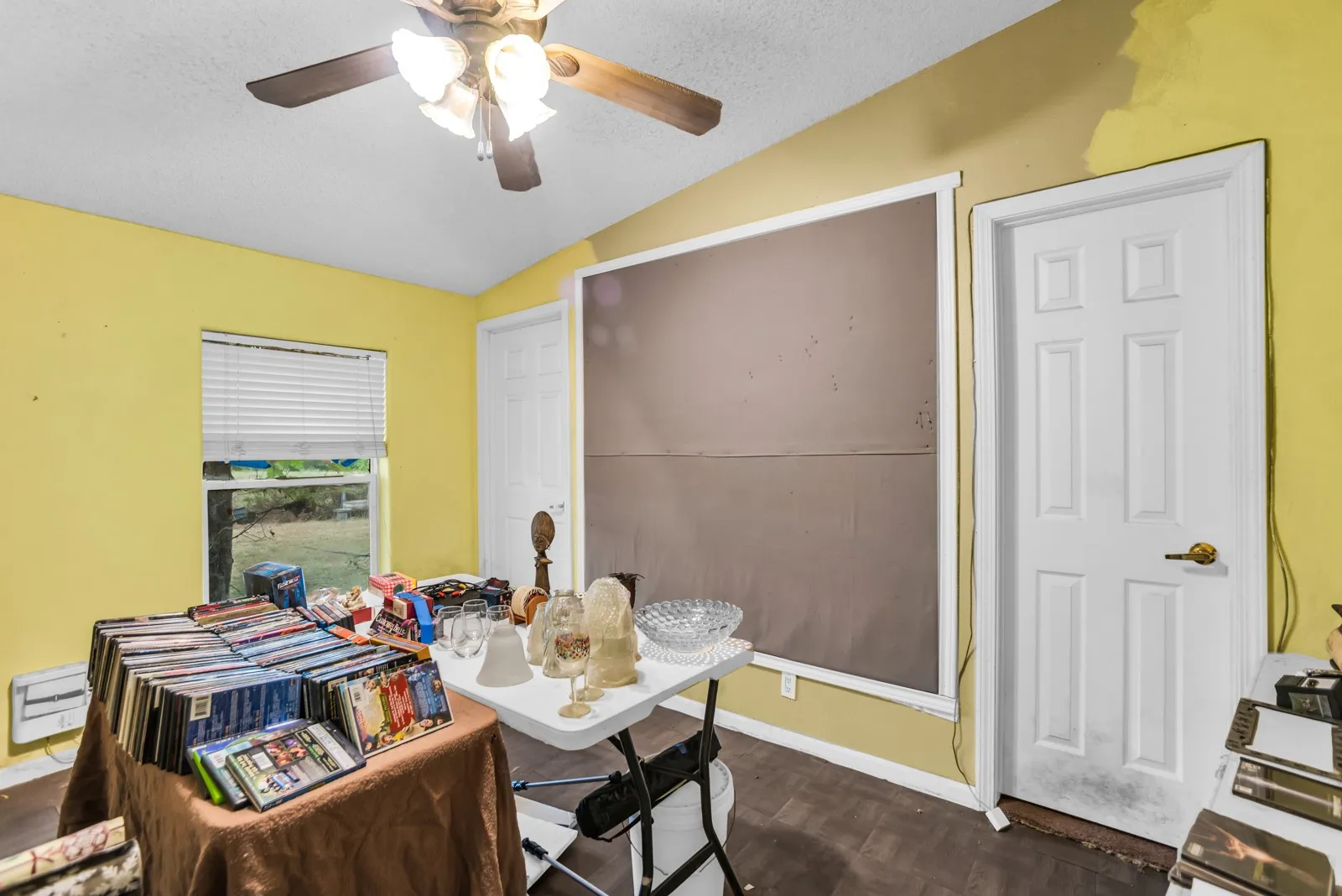 Vaulted ceiling, wood-finish flooring, white paneled doors, ceiling fan with integrated lighting, and a window with blinds
