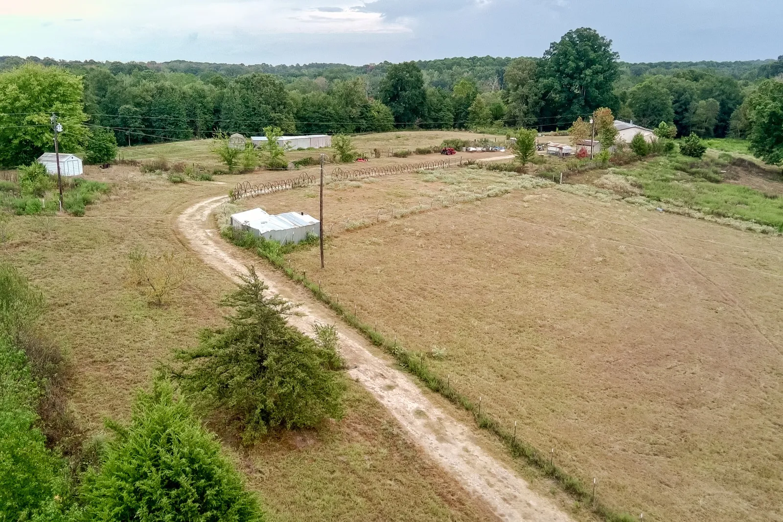 Expansive property featuring a gravel driveway, multiple outbuildings, and extensive open fields bordered by mature trees