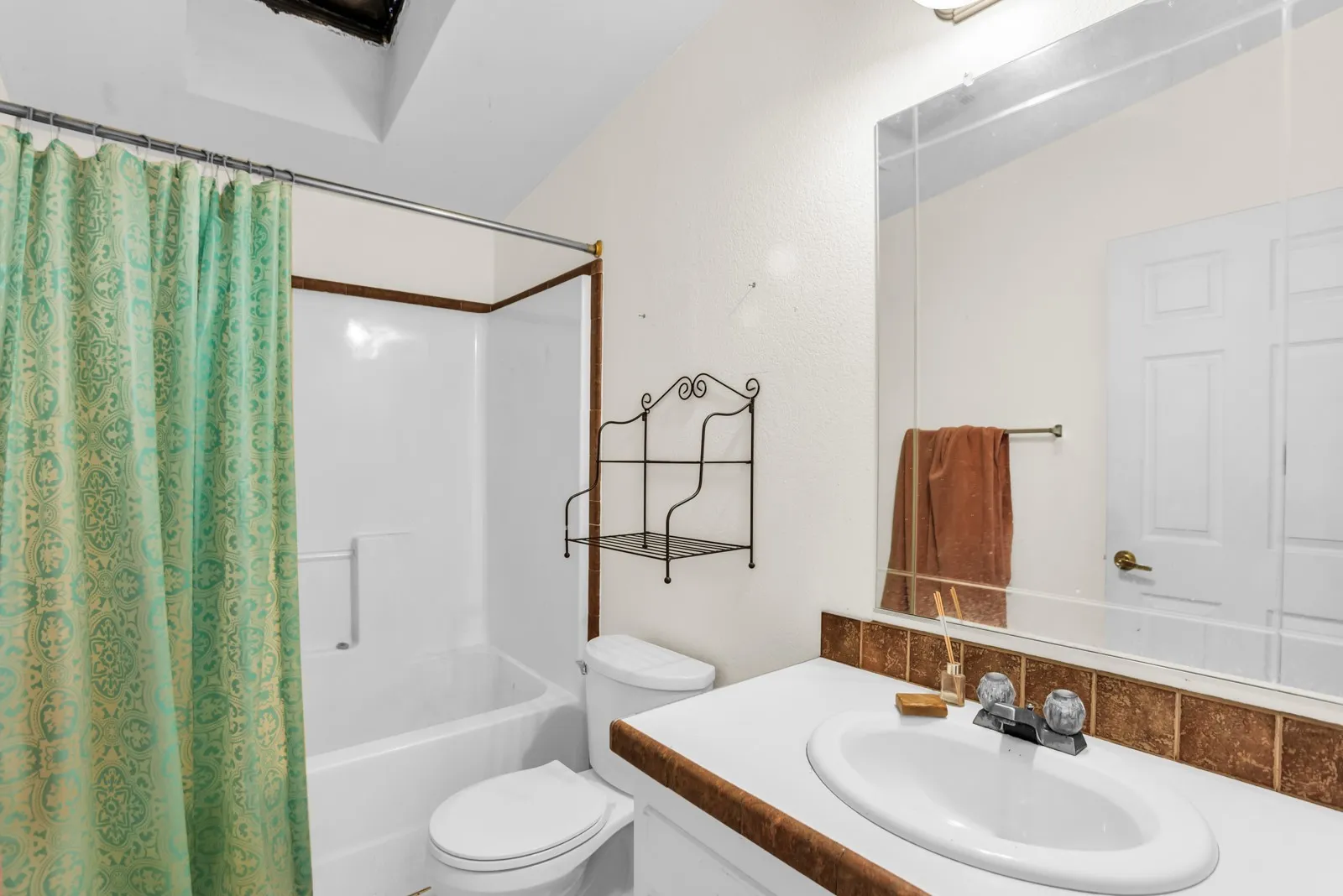 White bathtub with integrated shower, white toilet, and a vanity with a white countertop and tile backsplash