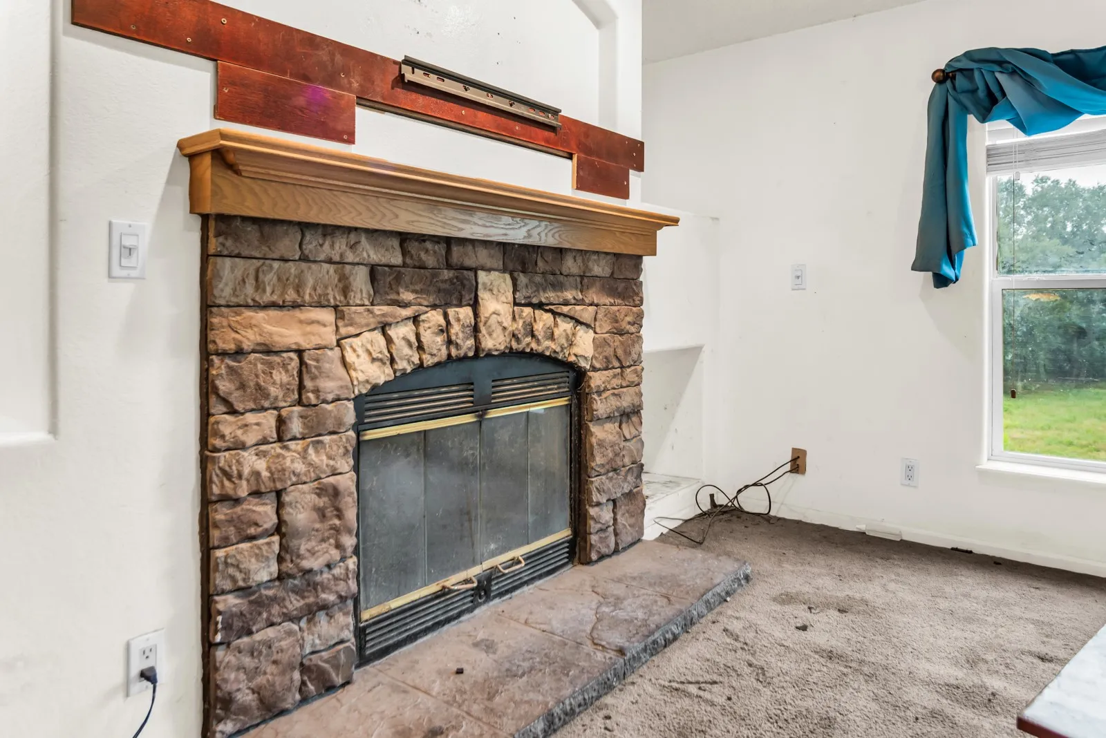 Stone-clad fireplace featuring an arched firebox with glass doors, a wood mantle, and a stone hearth