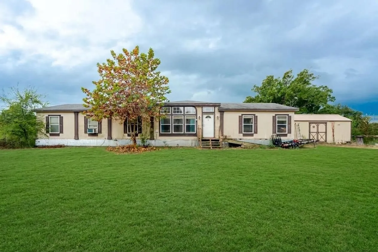 Expansive green lawn, light-colored siding, dark window shutters, multiple windows, and a detached outbuilding