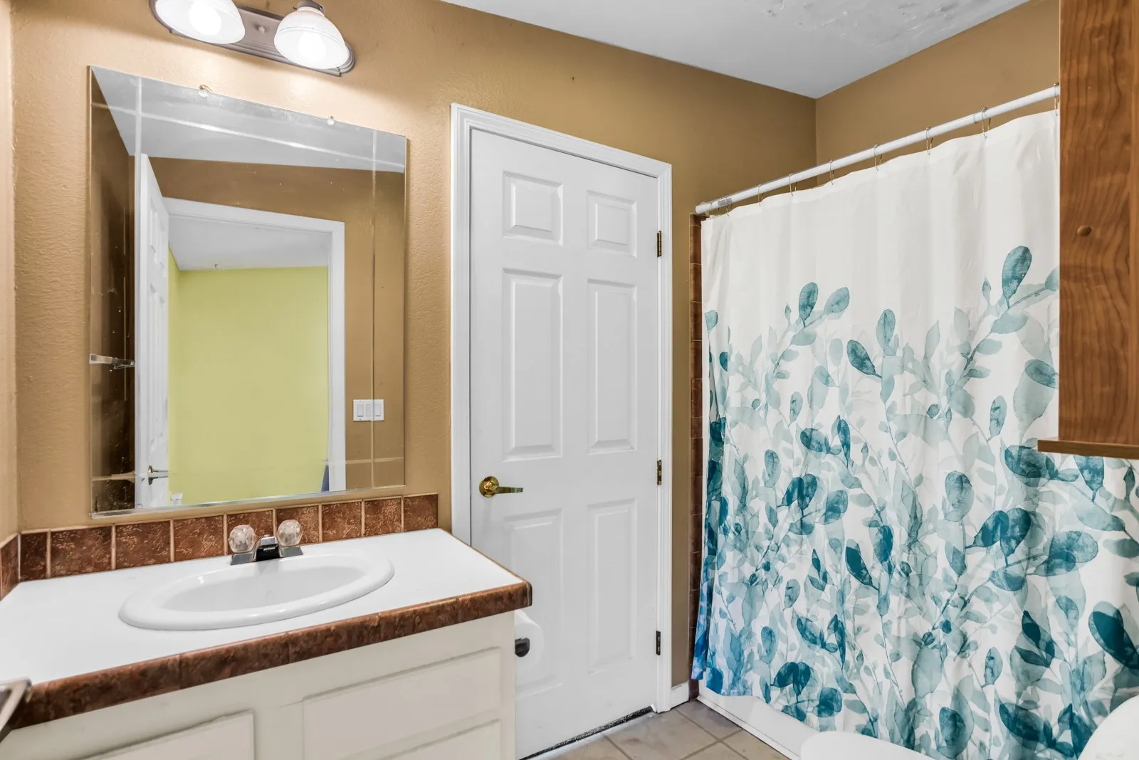 Vanity with integrated sink, tiled countertop, wall-mounted mirror, and overhead lighting fixture