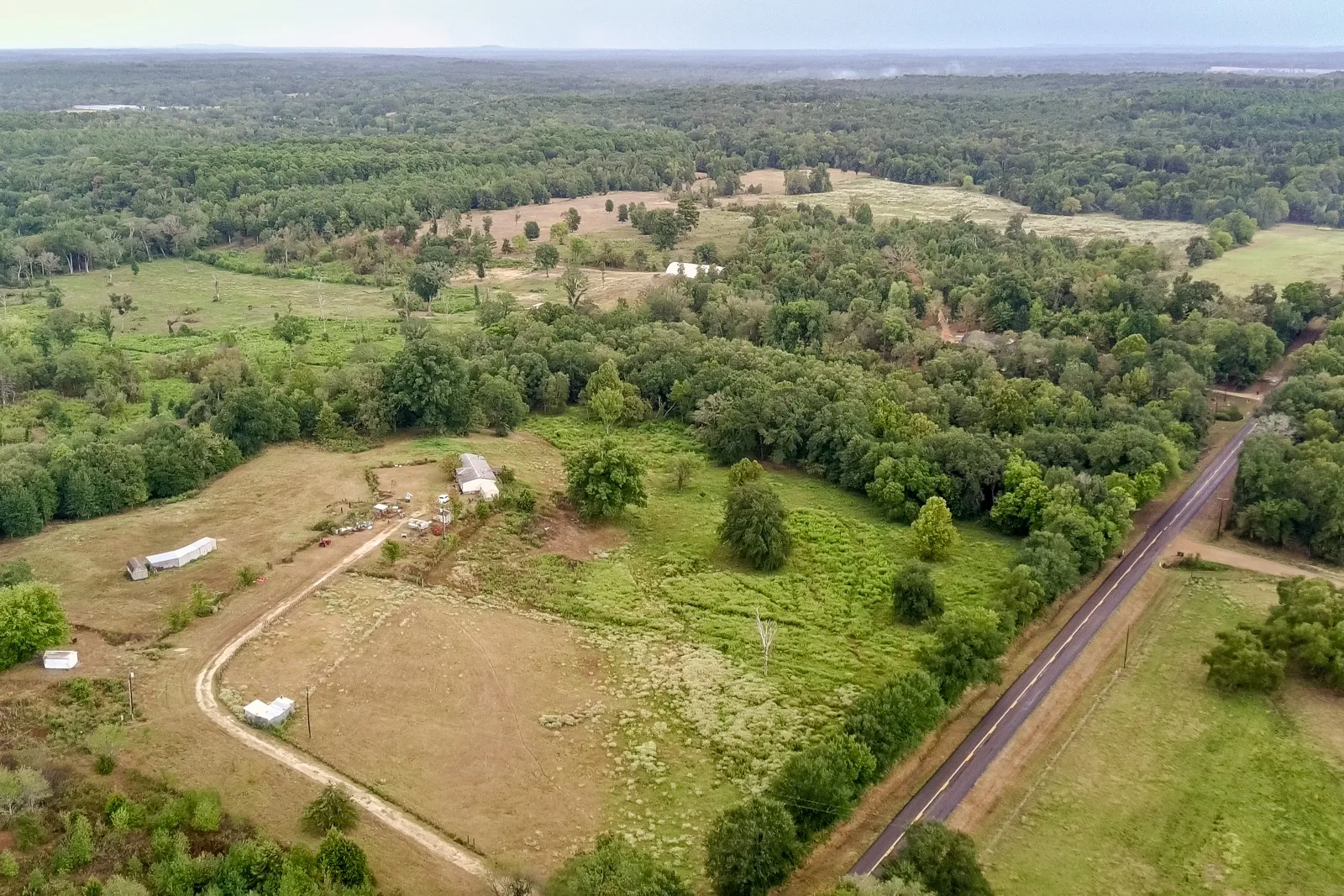 Expansive rural property featuring a paved road frontage, natural tree lines, and open cleared areas
