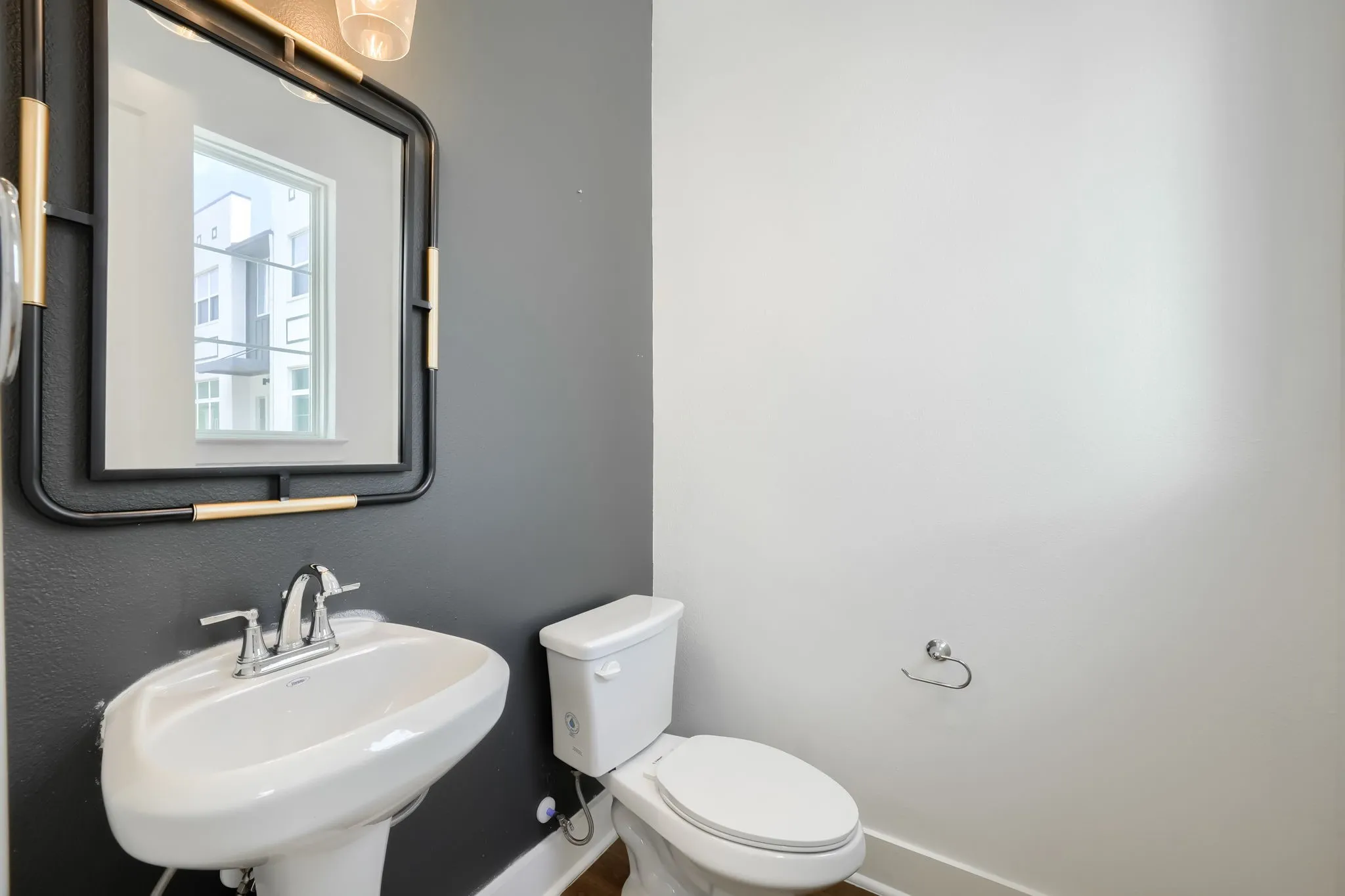 Pedestal sink with chrome faucet, wall-mounted mirror with gold-tone accents, and a white toilet