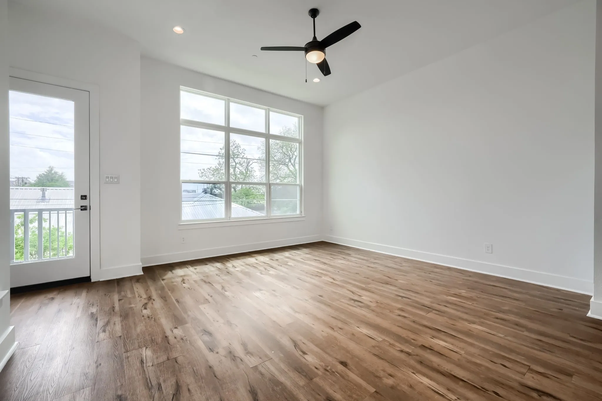Wood-finish flooring, a ceiling fan with integrated lighting, recessed ceiling lights, a multi-pane window, and a glass-paneled door