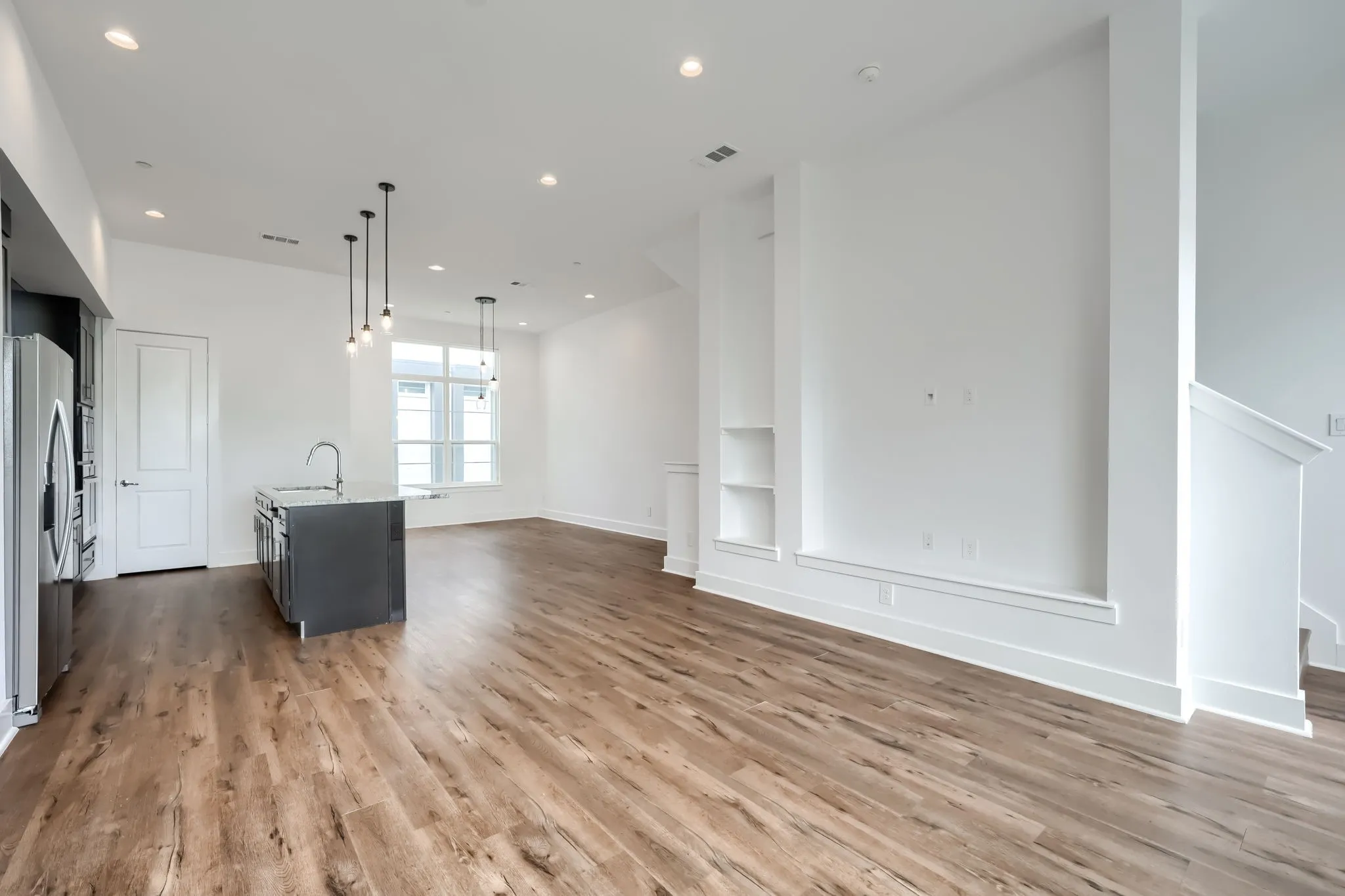 Open-concept living space with wood-finish flooring, recessed lighting, and a kitchen island featuring a stainless steel sink