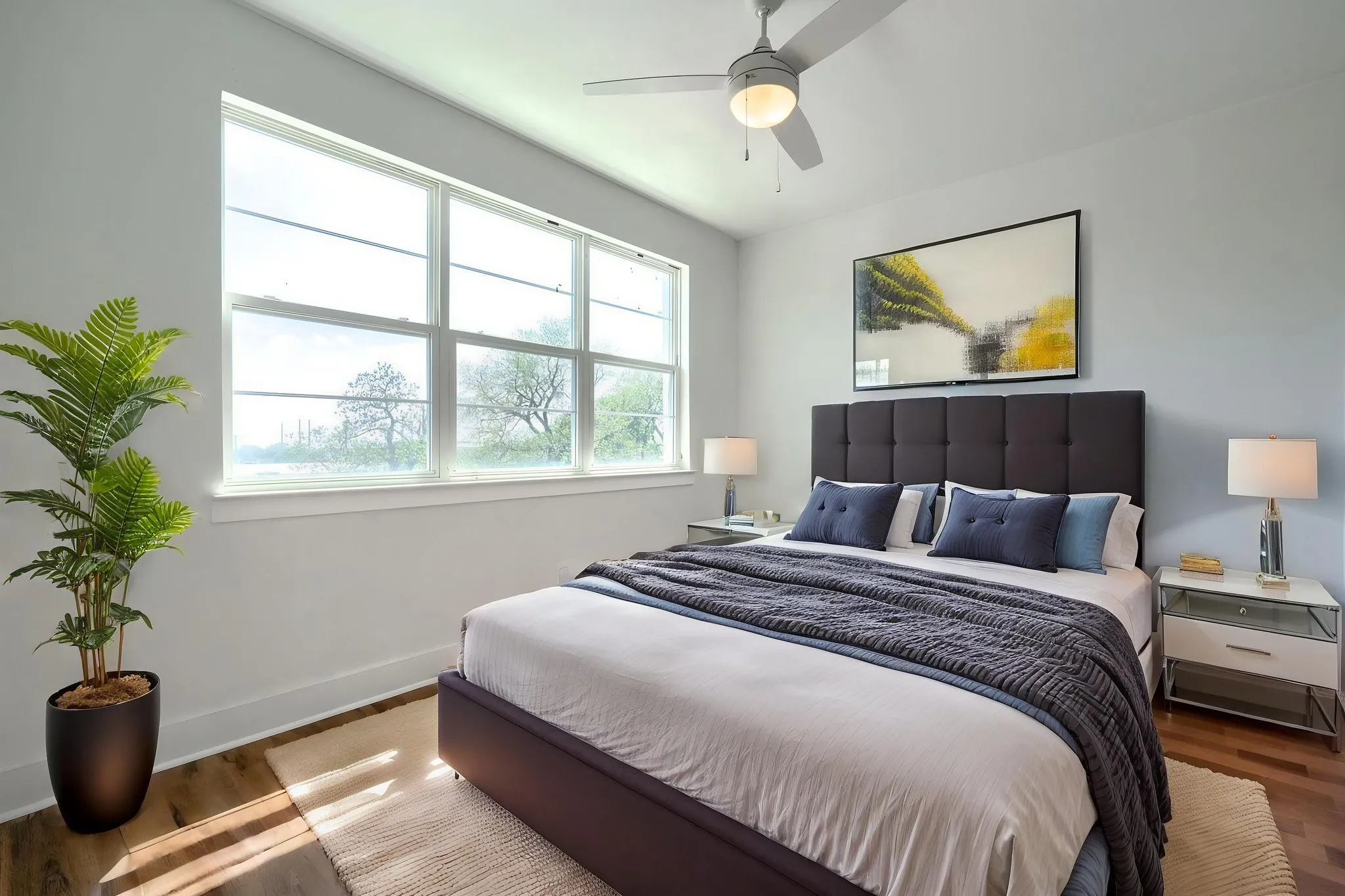Expansive windows with a serene outdoor backdrop, wood-finish flooring, and a ceiling fan