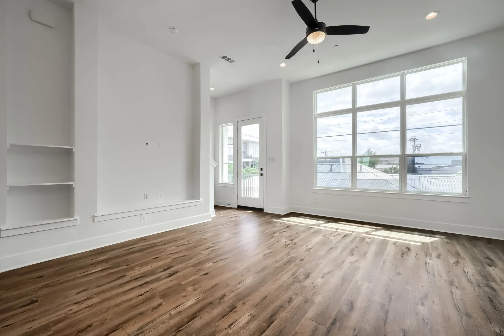 Spacious interior featuring wood-finish flooring, a large multi-pane window, built-in shelving, a ceiling fan, and recessed lighting