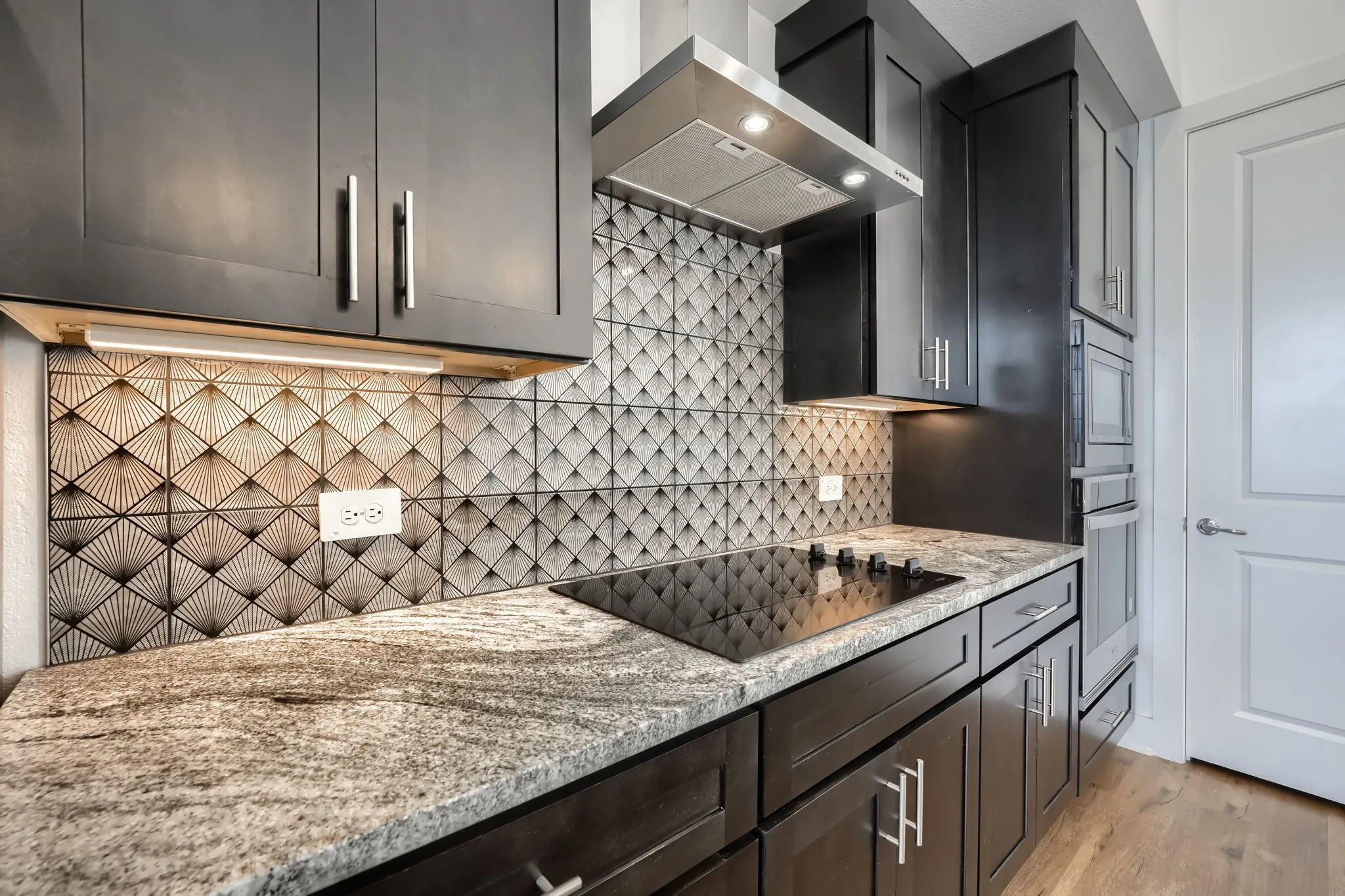 Dark wood-finish cabinetry, built-in stainless steel appliances, granite countertops, patterned tile backsplash, and a black induction cooktop