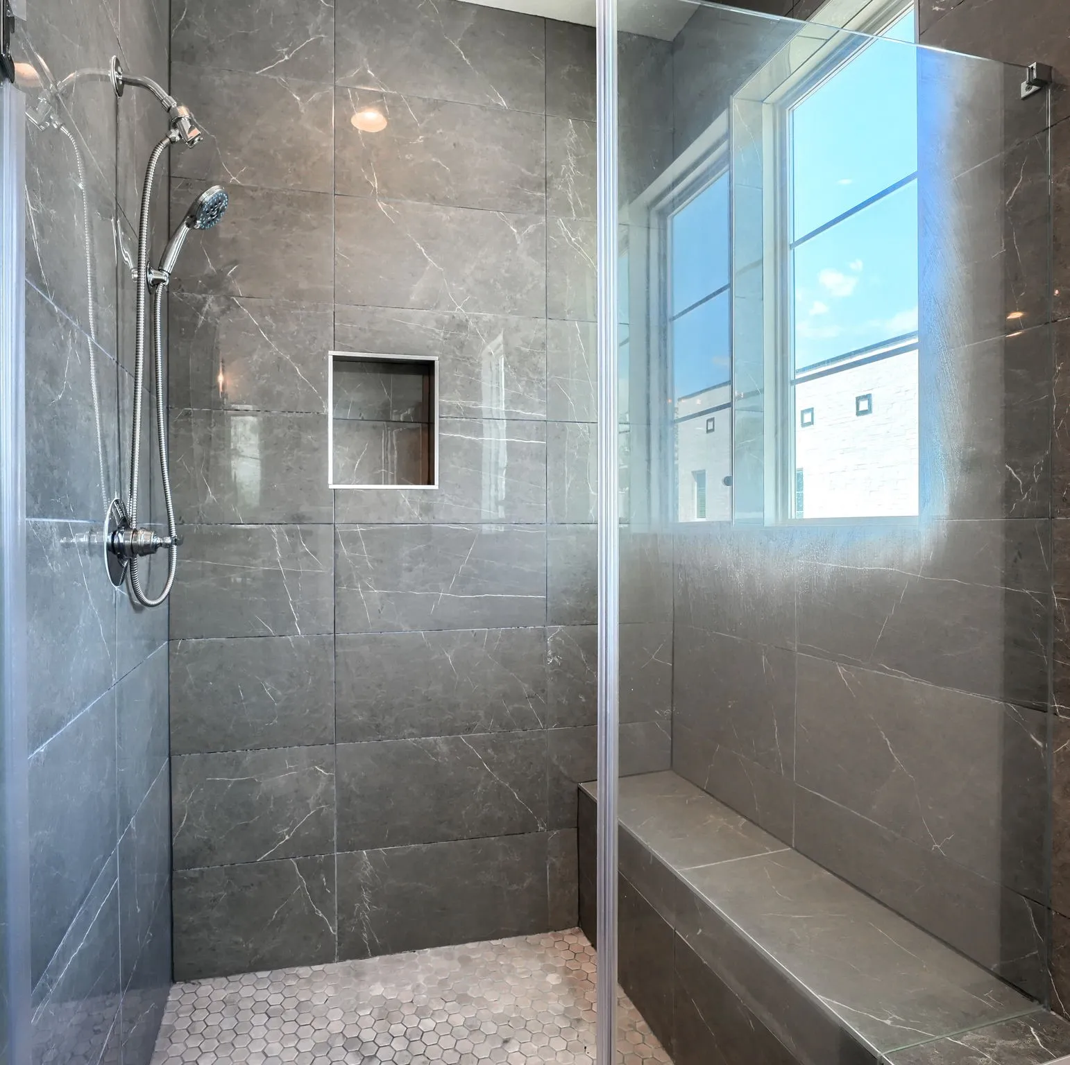 Walk-in shower featuring full-height stone-look tile, a built-in bench, a window, a recessed niche, and a handheld shower fixture