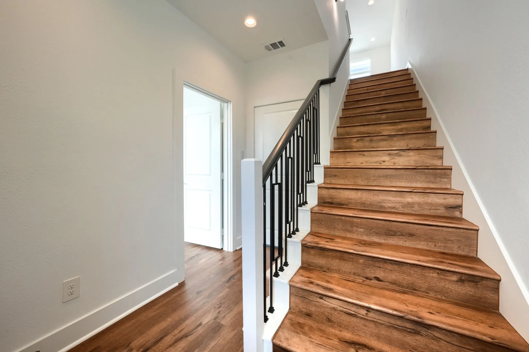 Wood-finish flooring throughout, featuring a staircase with black metal balusters and a white newel post