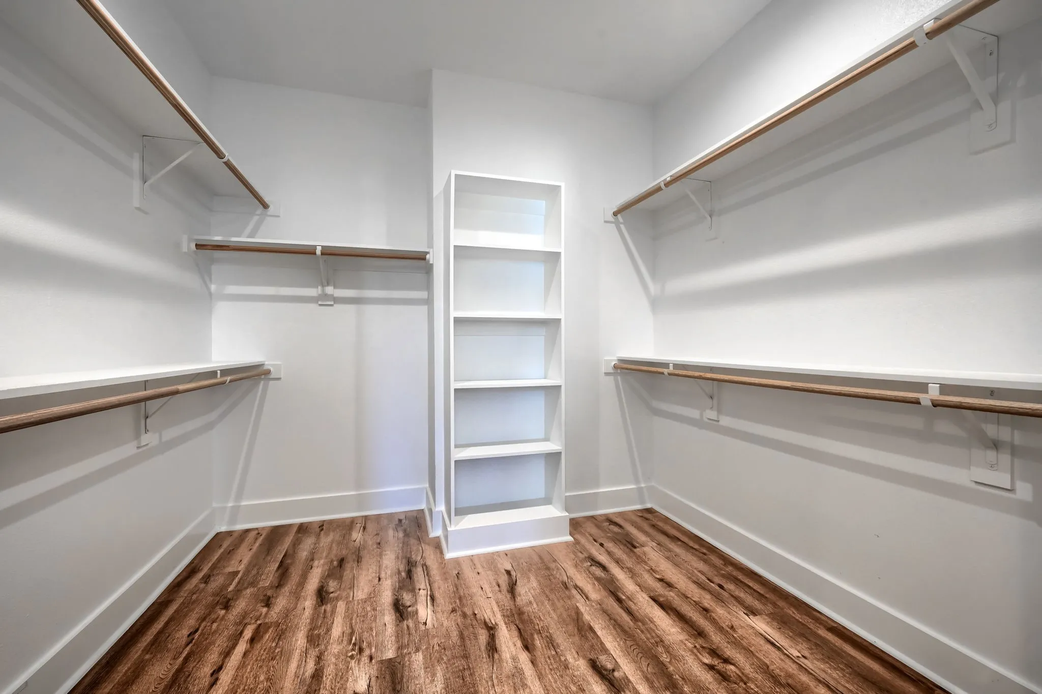 Spacious walk-in closet featuring wood-finish flooring, white walls, built-in shelving unit, and multiple hanging rods with shelving
