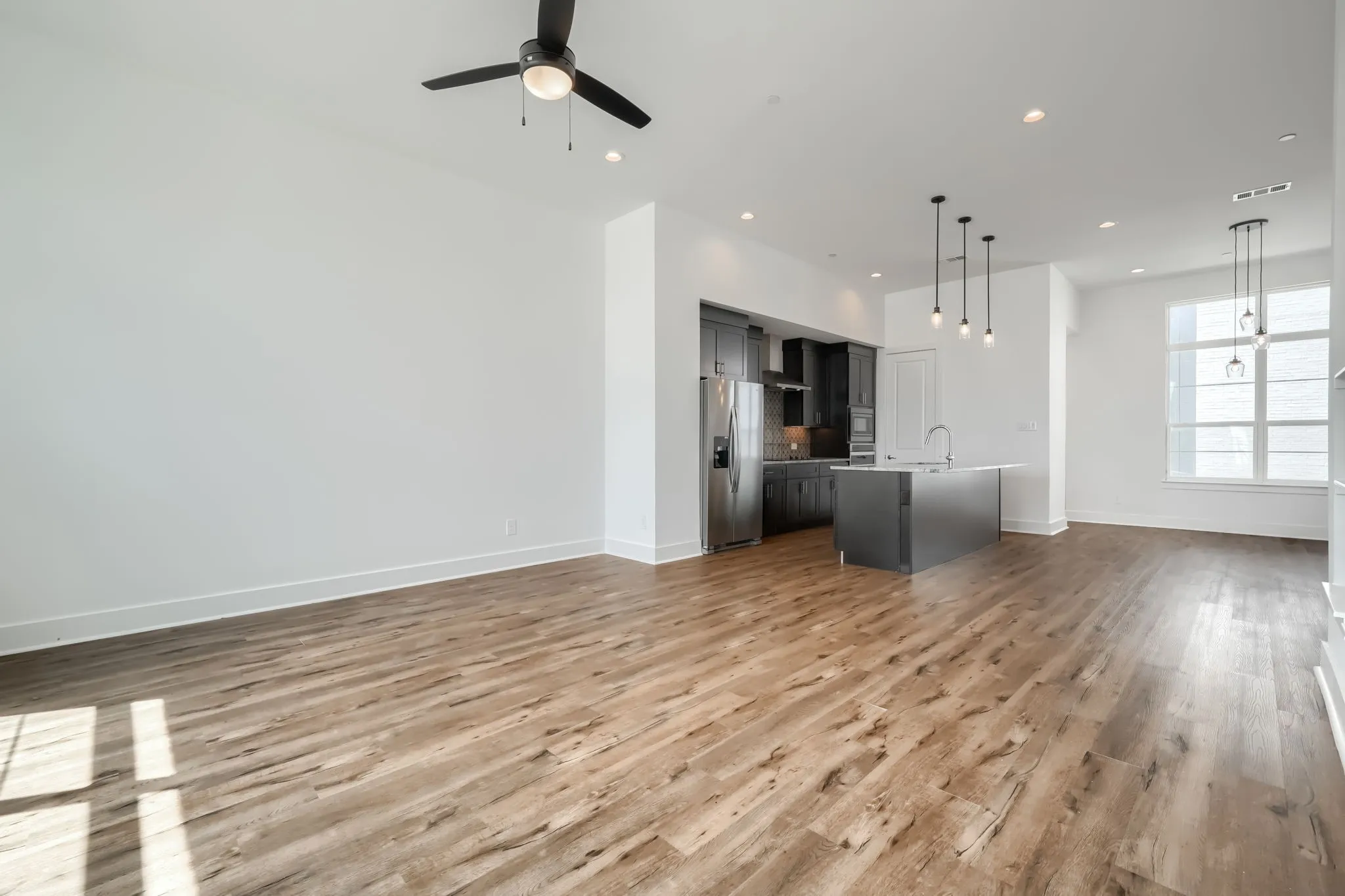 Open-concept living area with wood-finish flooring, a contemporary kitchen, stainless steel appliances, and abundant natural light from large windows