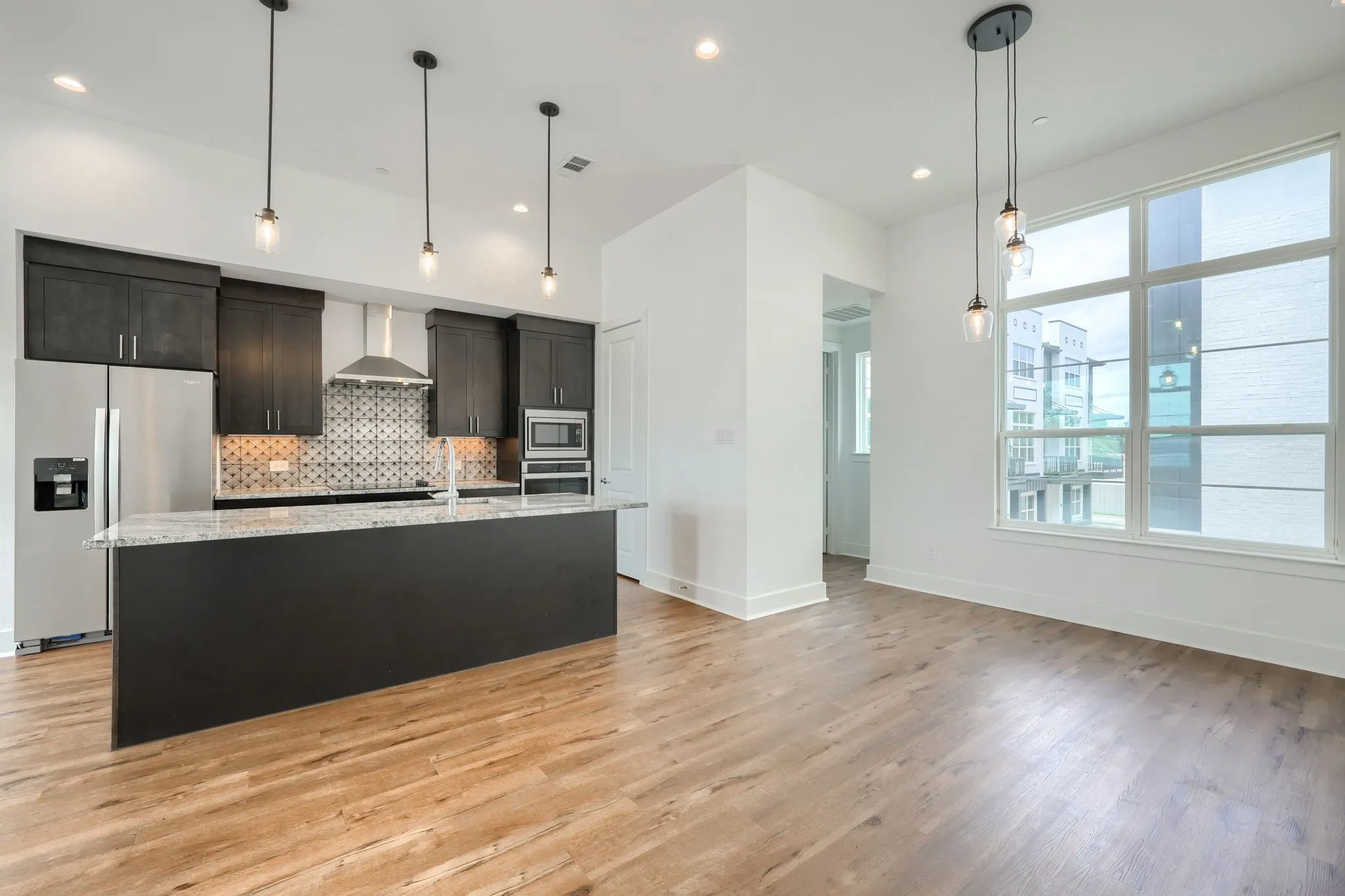 Open-concept living area featuring wood-finish flooring, a kitchen island with a light-toned countertop, stainless steel appliances, and a geometric tile backsplash