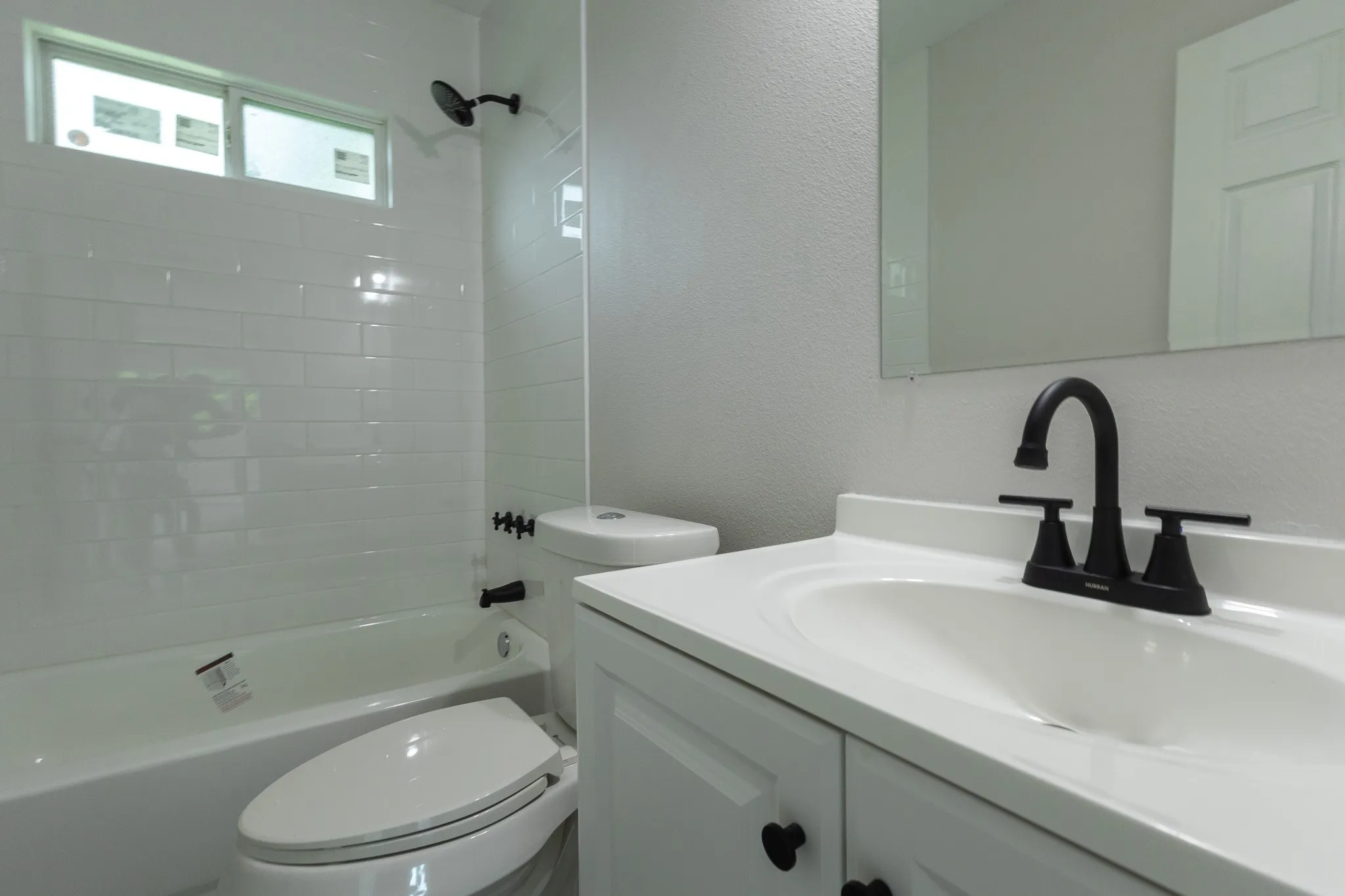 White subway tile shower surround, matte black fixtures, white vanity with integrated sink, and a rectangular wall mirror