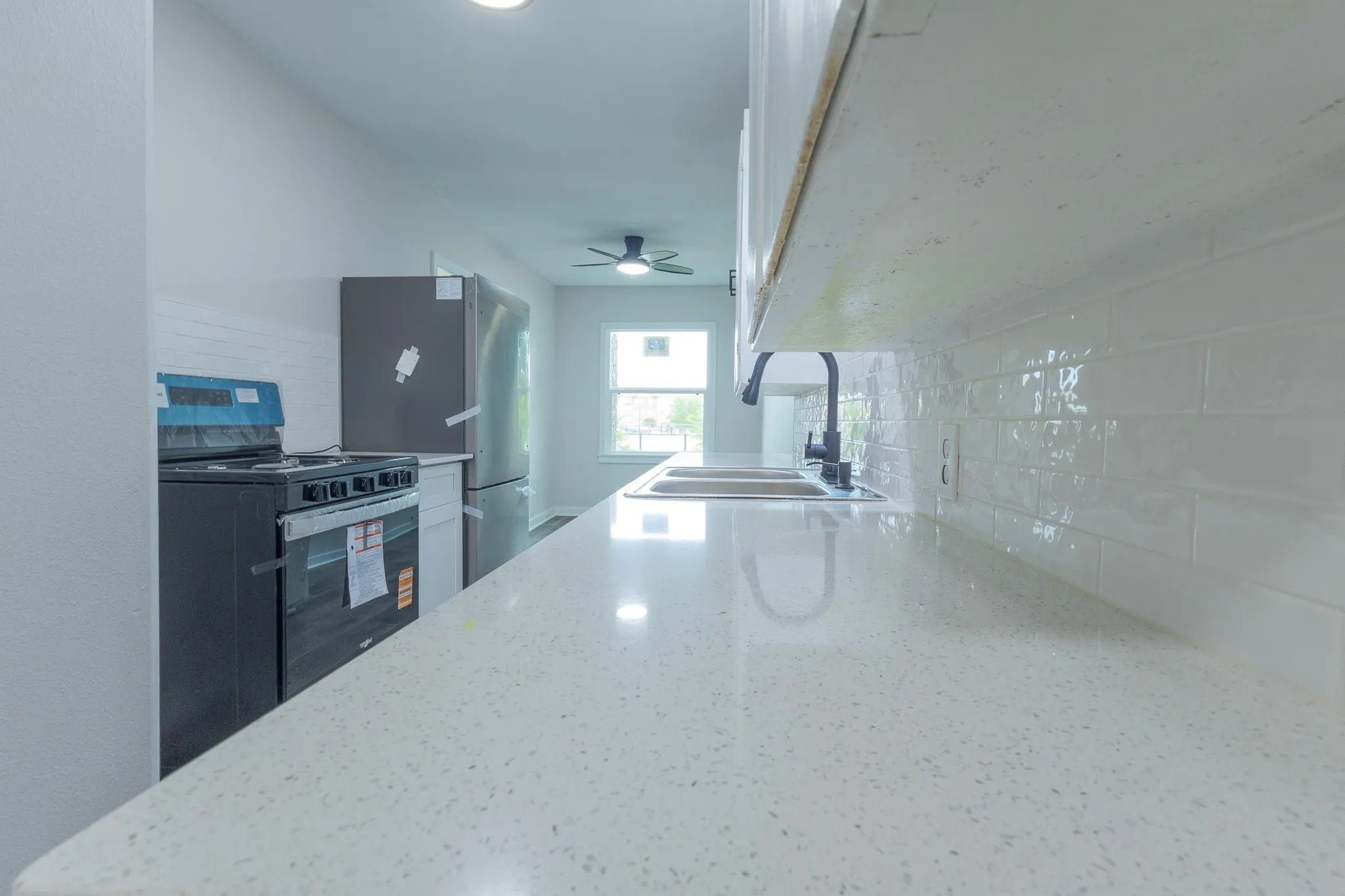 White solid surface countertops, subway tile backsplash, stainless steel refrigerator, black range, and dual basin sink with black hardware
