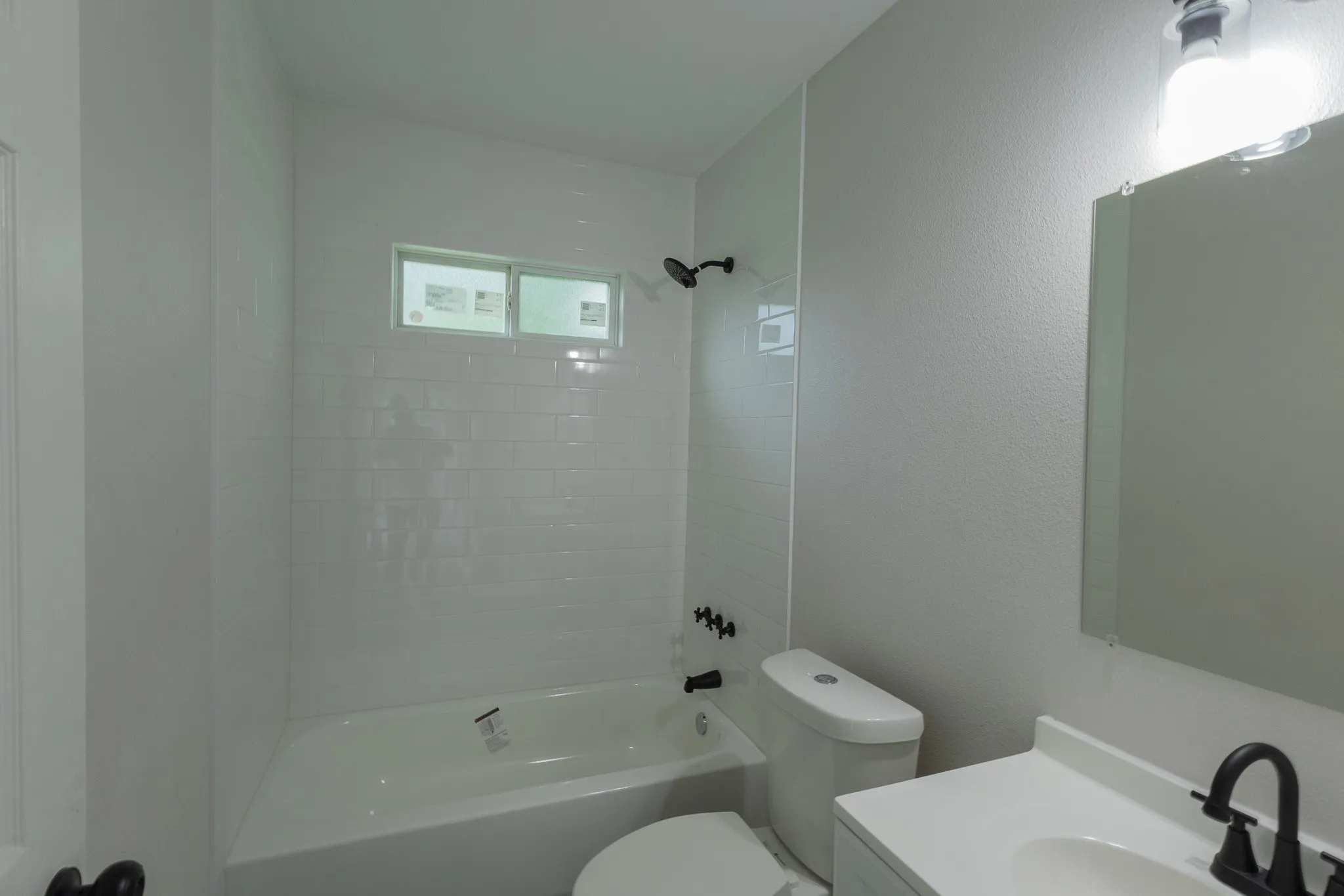 White subway tile shower surround with a built-in tub, black shower fixtures, vanity with integrated sink, and wall-mounted mirror