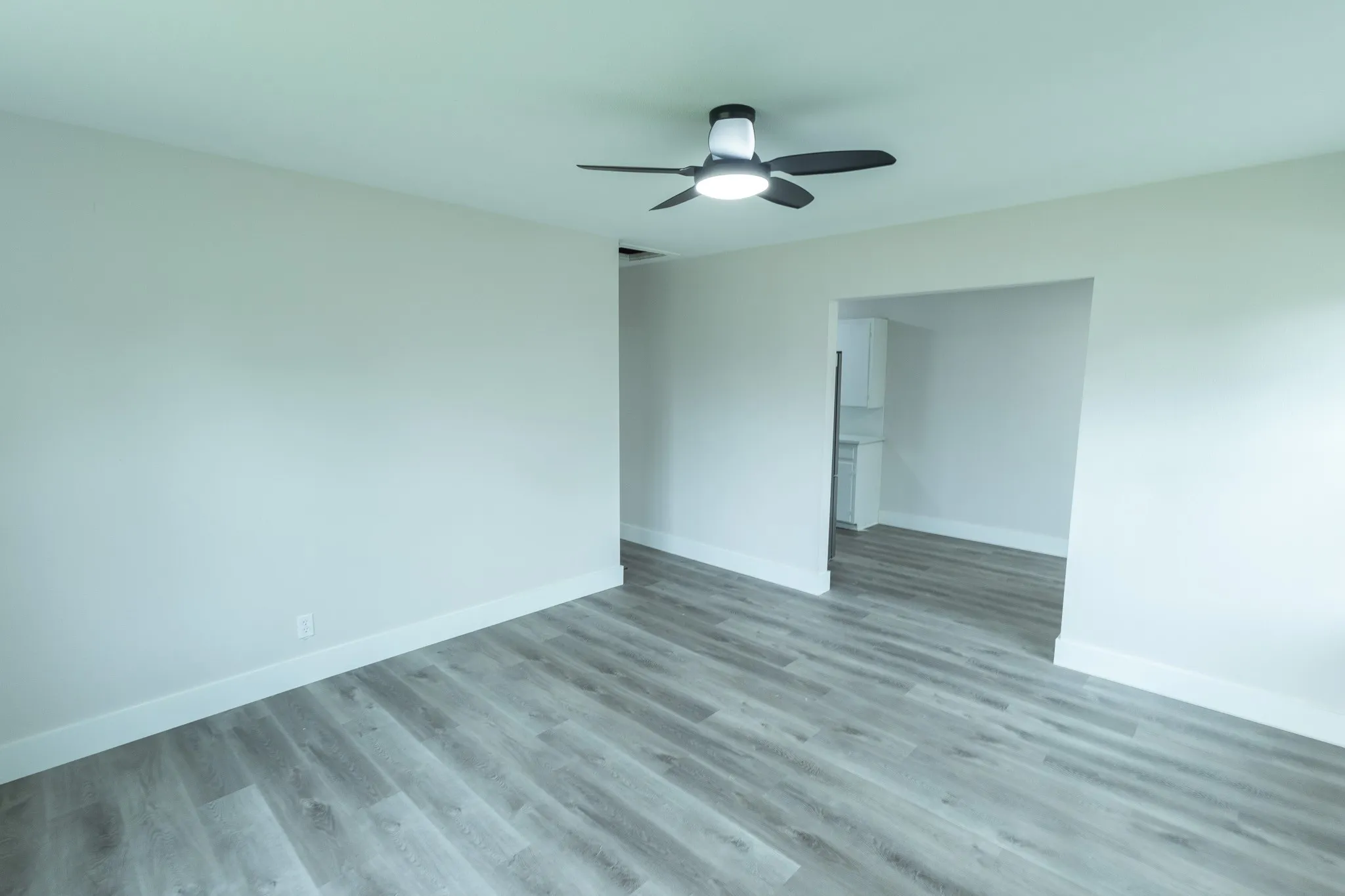 Wood-finish flooring throughout, bright white walls, and a contemporary ceiling fan with integrated lighting