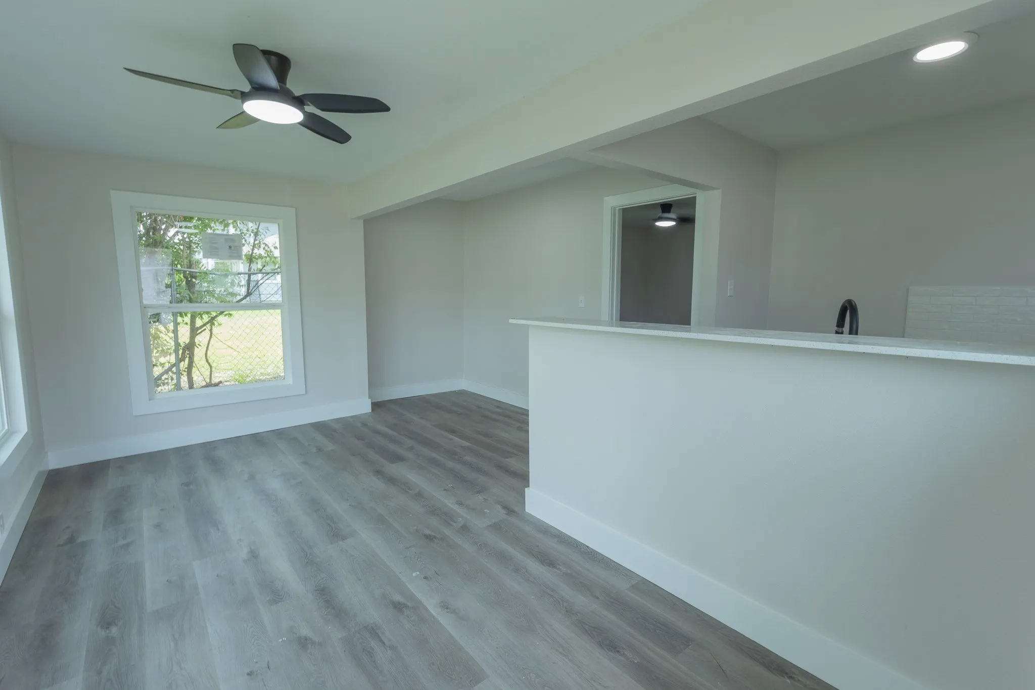 Open-concept living space featuring wood-finish flooring, a contemporary ceiling fan, and a pass-through counter with a sink