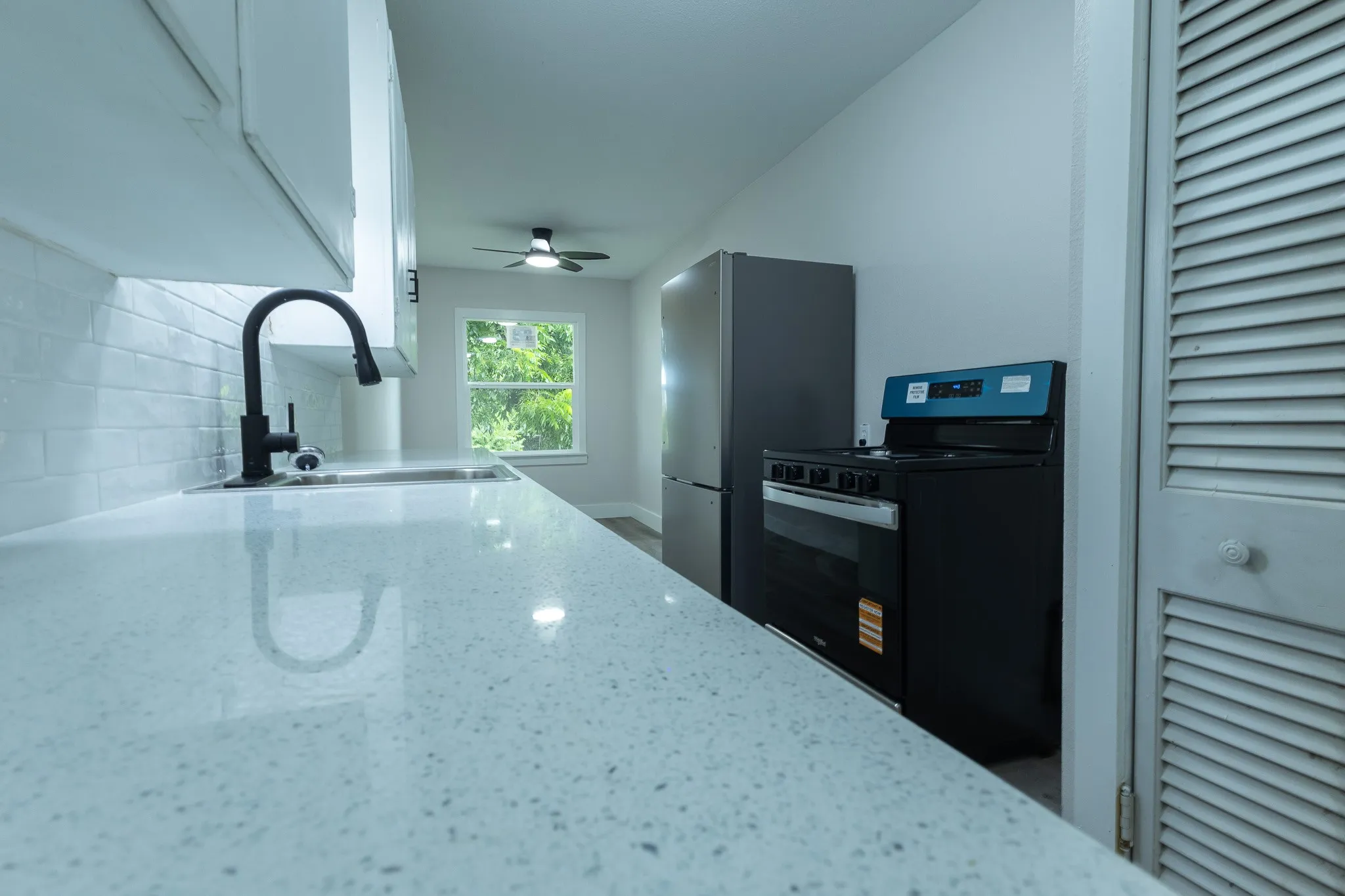 Kitchen featuring a stainless steel sink, matte black faucet, subway tile backsplash, white cabinetry, and light-toned countertops