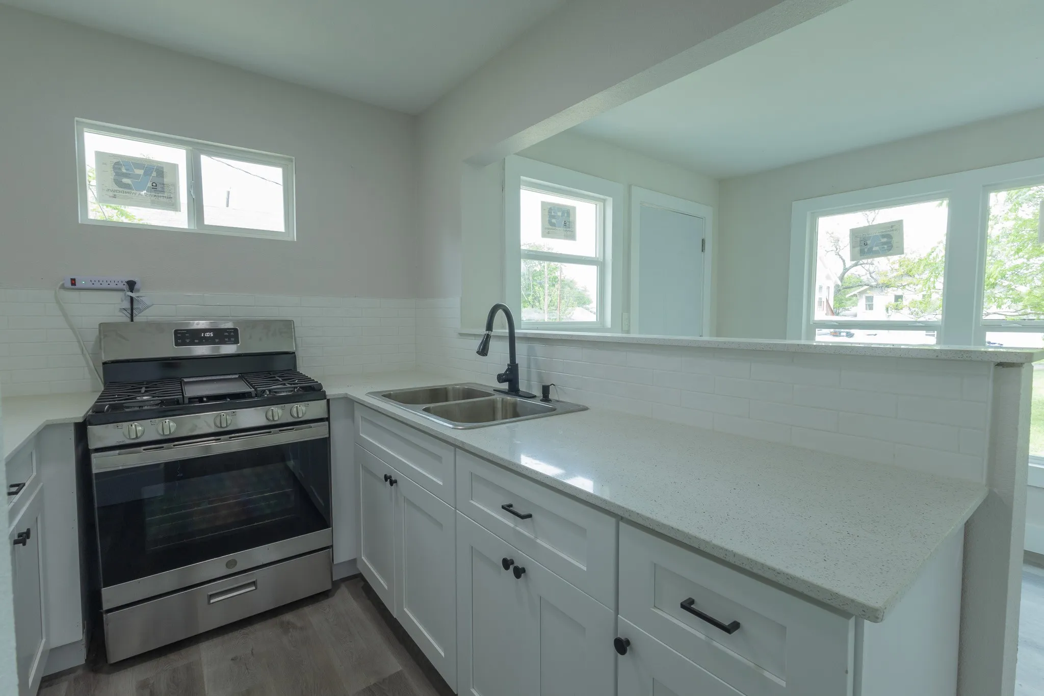 Modern kitchen featuring stainless steel gas range with multiple burners, white cabinetry with hardware accents, quartz countertops, undermount sink with contemporary faucet, and abundant natural light from multiple windows