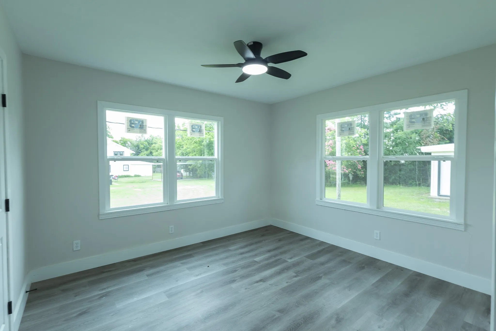 Room featuring wood-finish flooring, two large windows, a ceiling fan with integrated lighting, and light-toned walls