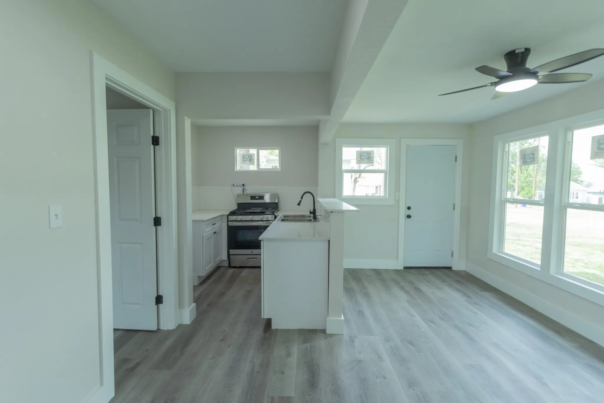 Open-concept living space featuring wood-finish flooring, a ceiling fan, and multiple large windows