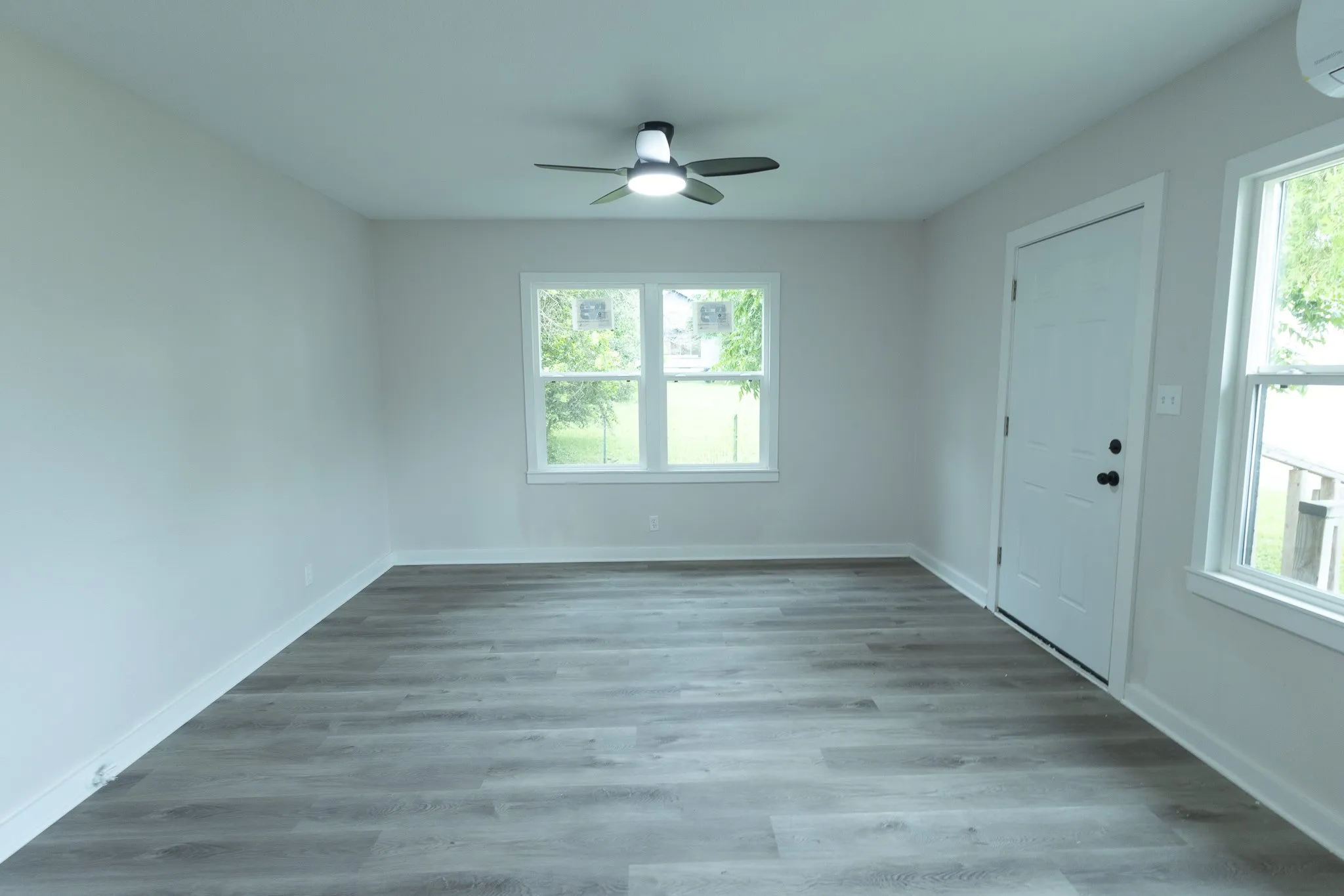 Bright, light-filled bedroom showcasing wood-finish flooring, ceiling fan with integrated lighting, and multiple windows providing natural illumination