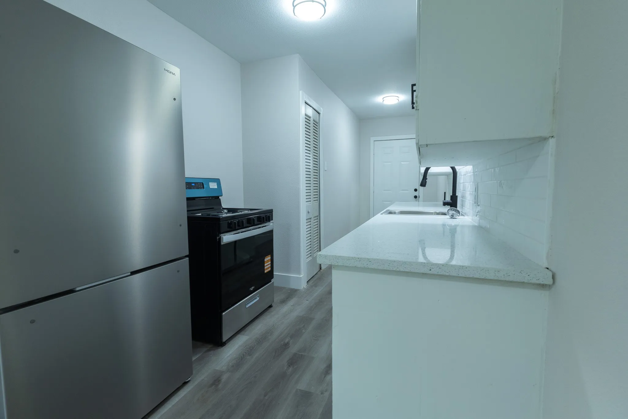 Stainless steel refrigerator and range, white shaker-style cabinetry, solid surface countertops, white subway tile backsplash, and wood-finish flooring