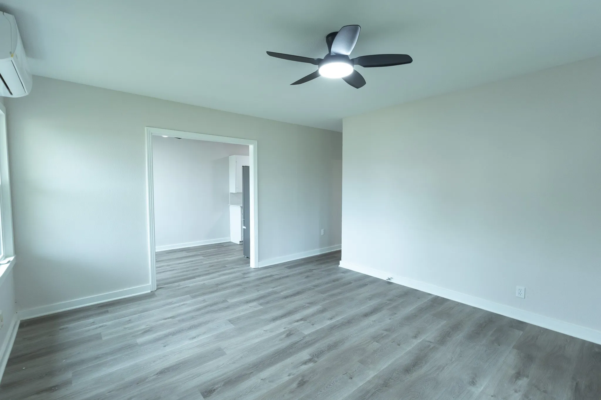 Wood-finish flooring, ceiling fan with integrated lighting, white trim, and a wall-mounted climate control unit