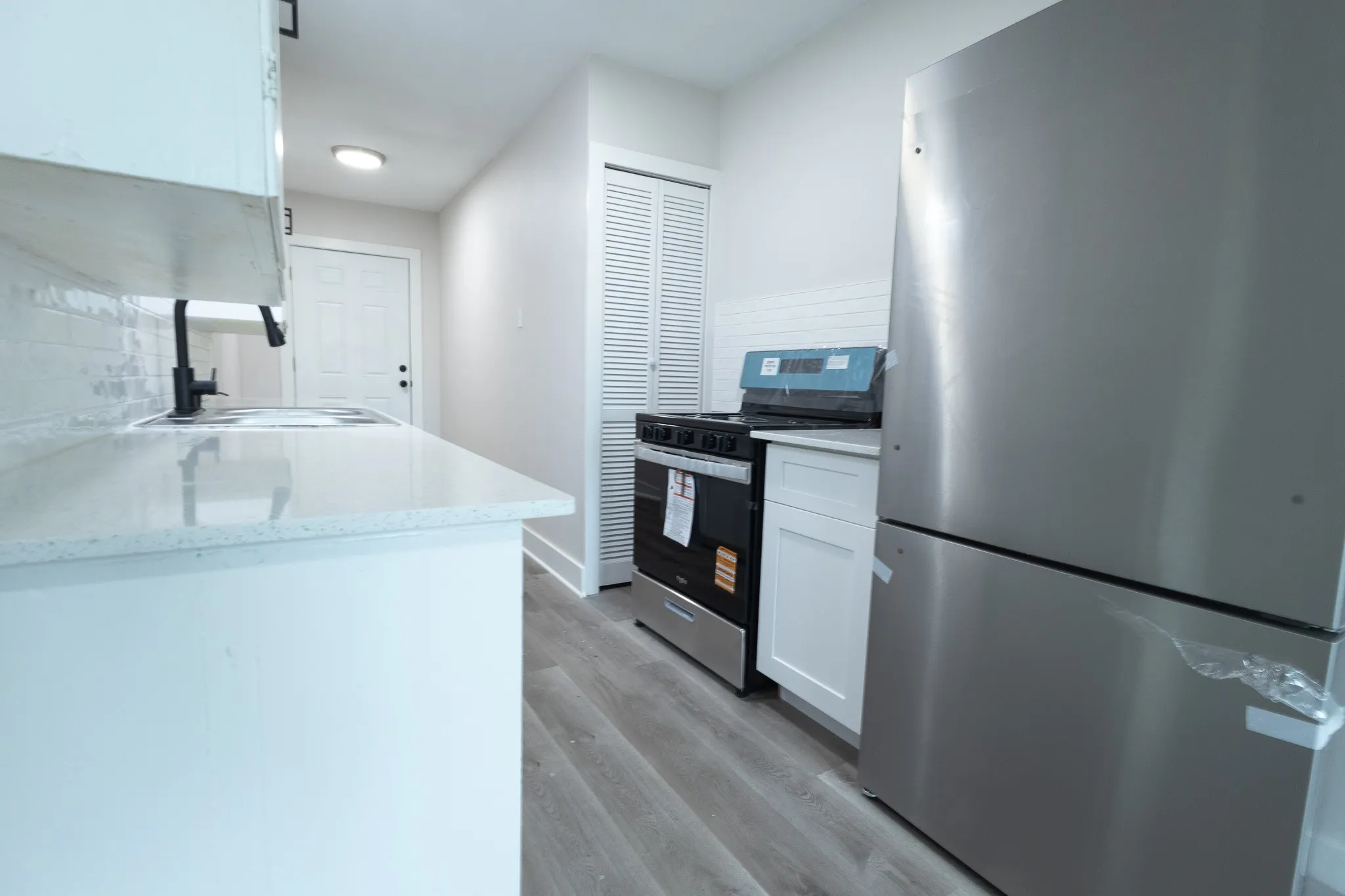 Kitchen featuring quartz countertops, white cabinetry, wood-finish flooring, a stainless steel refrigerator, and a black range