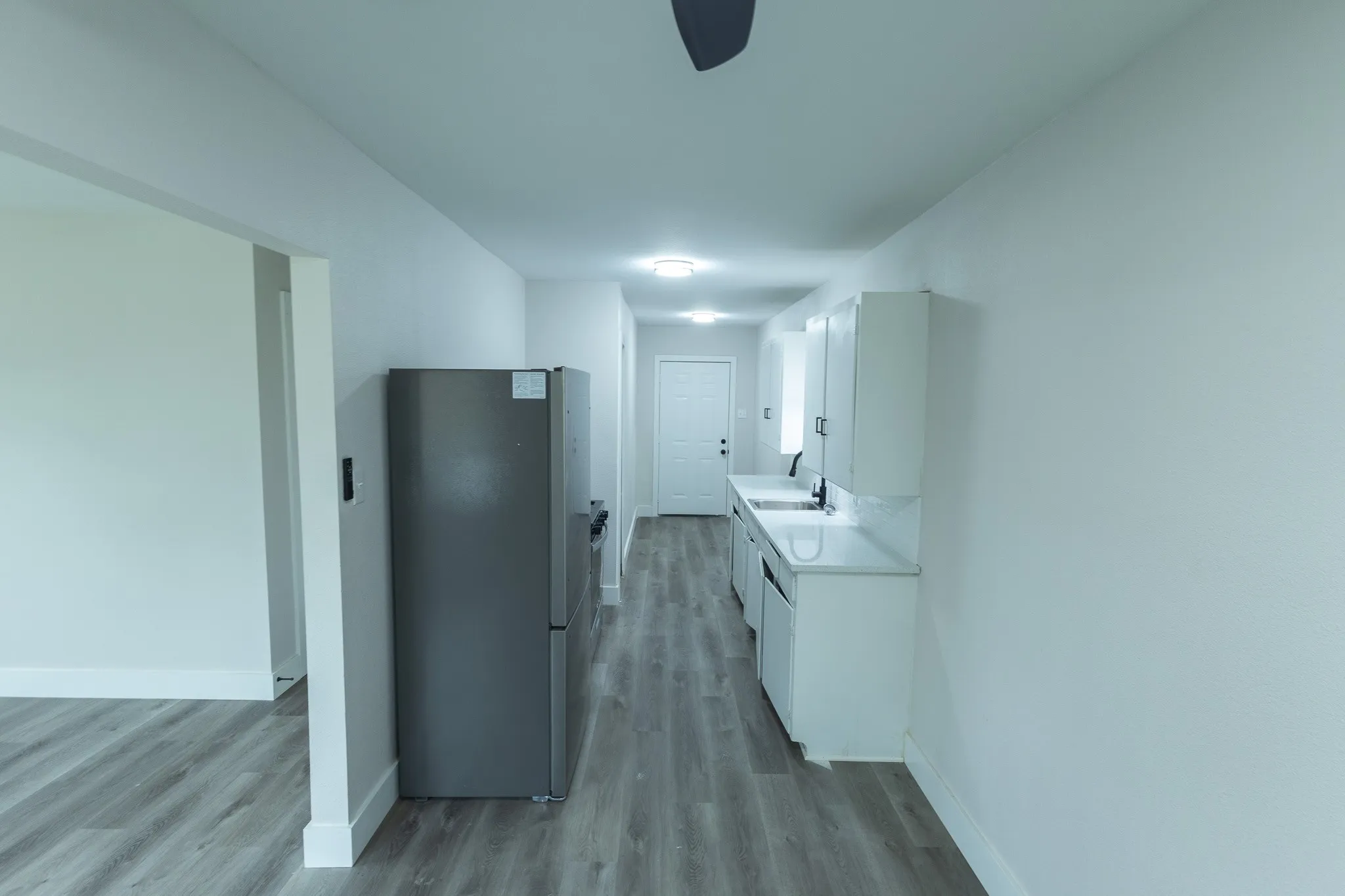 Galley kitchen featuring white cabinetry, light countertops, integrated sink, and stainless steel refrigerator