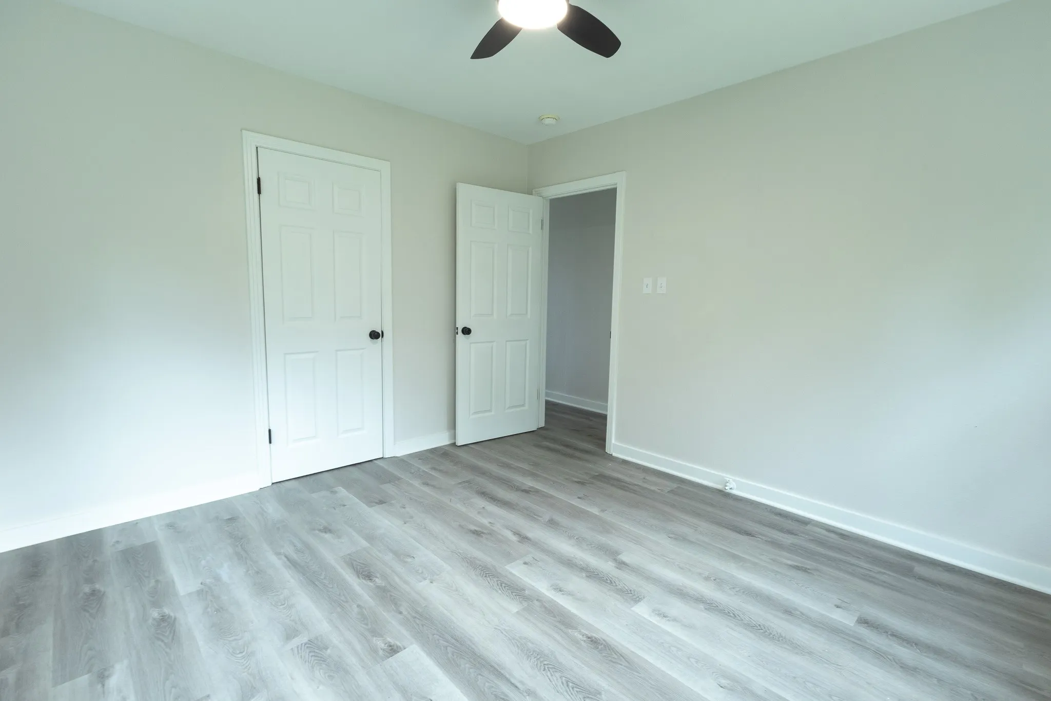 Wood-finish flooring throughout, light-toned walls, white trim, white interior doors, and a ceiling fan