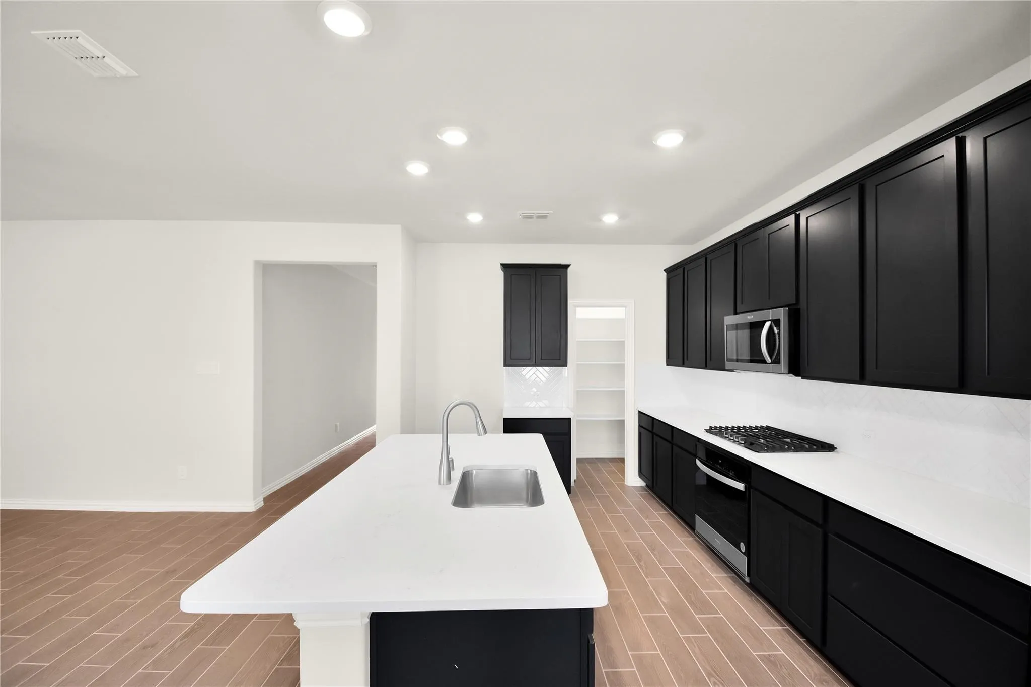 Modern kitchen featuring a large island with an undermount sink, white countertops, black cabinetry, and wood-finish flooring