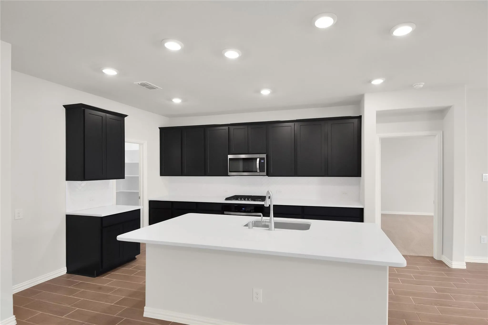 Kitchen featuring dark cabinetry, stainless steel appliances, a center island with sink, white countertops, and wood-finish flooring