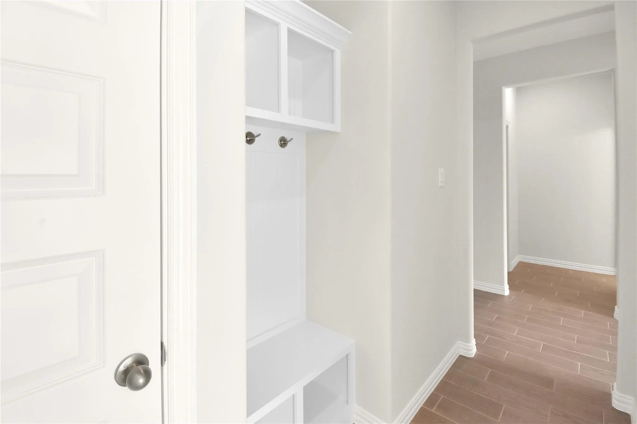 Built-in hall tree with storage cubbies and coat hooks, panel door, and wood-finish flooring