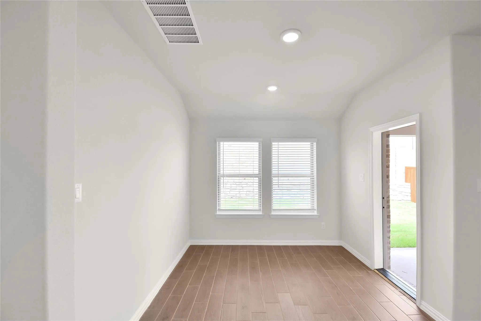 Wood-finish flooring with white baseboards, two windows with blinds, recessed lighting, and a glass-paneled door