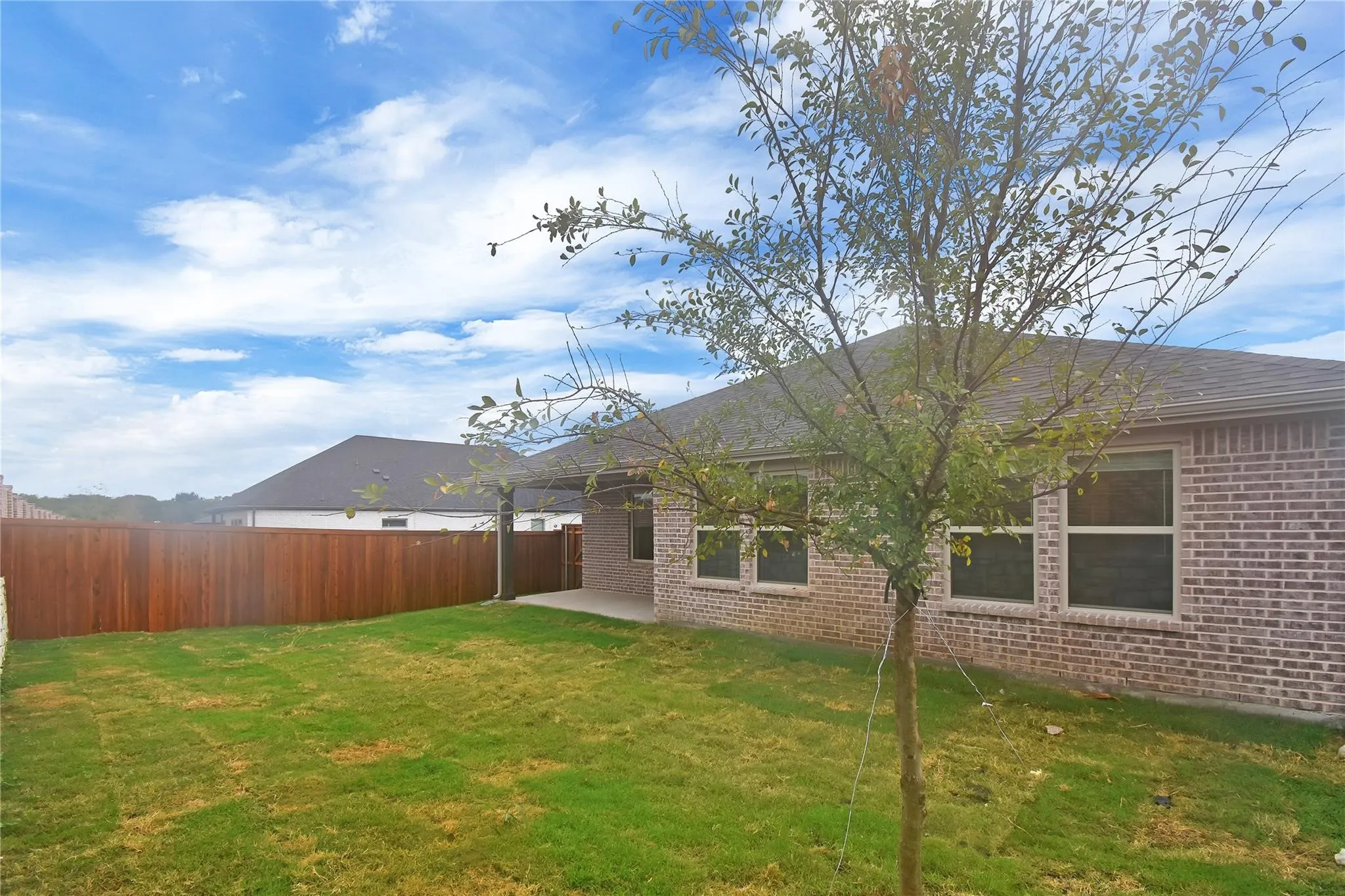Expansive grass lawn with a brick exterior, privacy fencing, multiple windows, and a covered patio