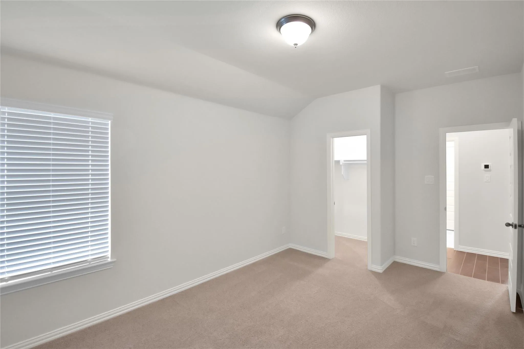 Vaulted ceiling, carpeted flooring, window with blinds, flush-mount lighting, and an open doorway leading to a closet