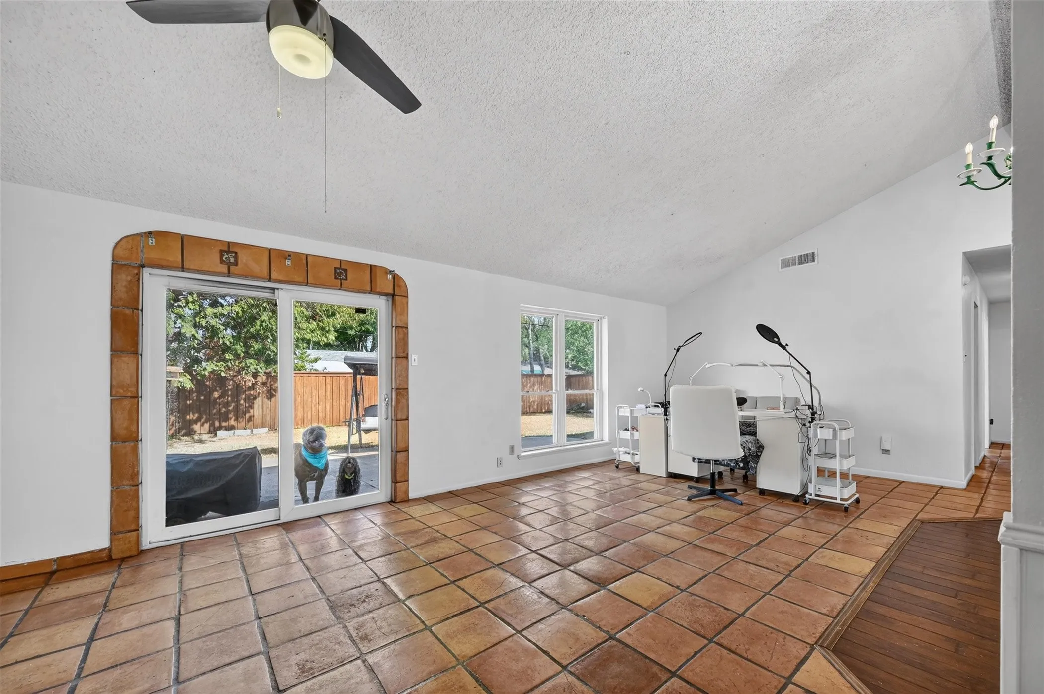 Vaulted ceiling with an attached ceiling fan, terra cotta tile flooring, white walls, and a sliding glass door